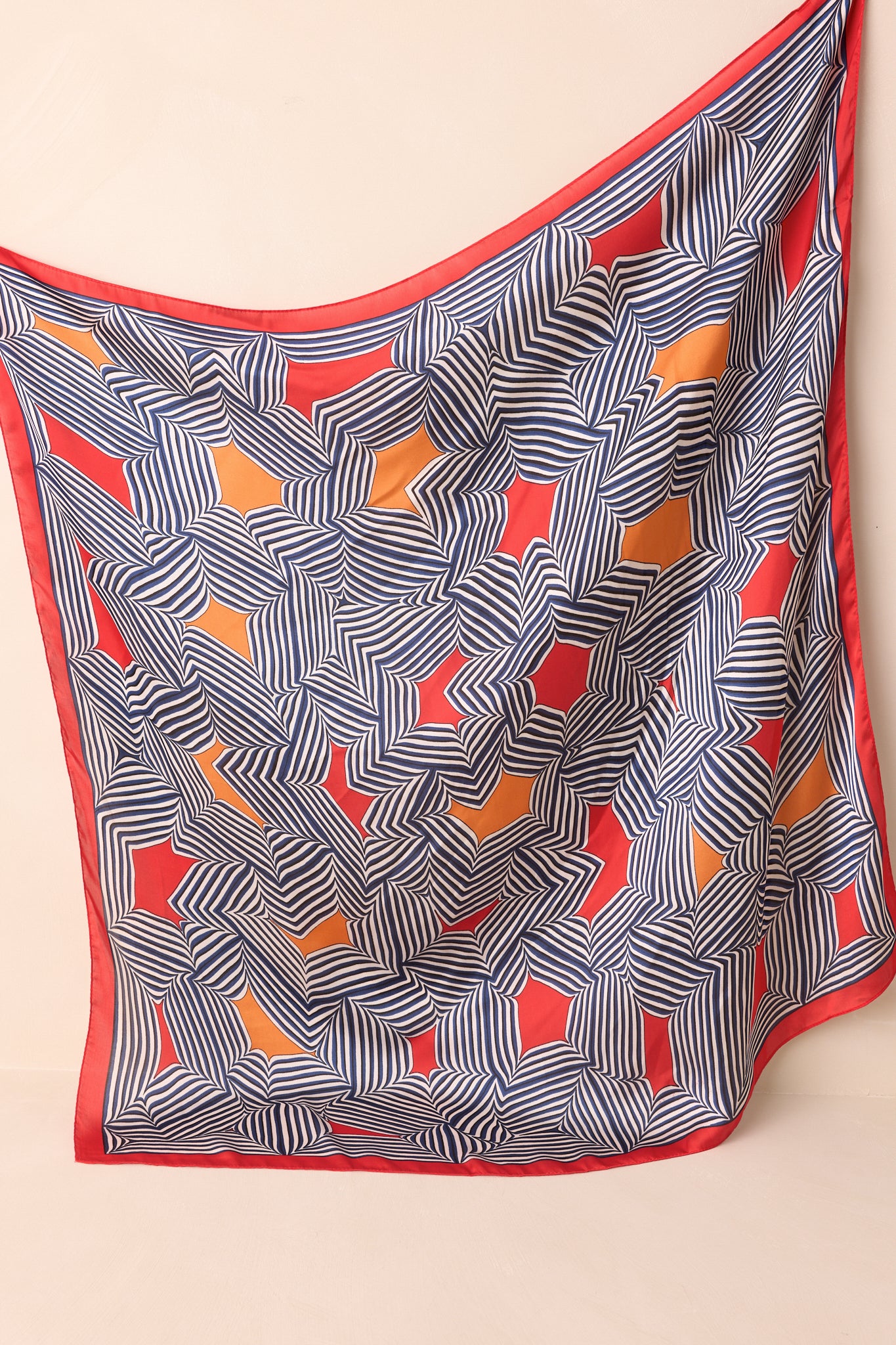 Full view of the large red scarf laid flat, featuring a bold stripe geometric print with orange and red color block details and a glossy satin finish.