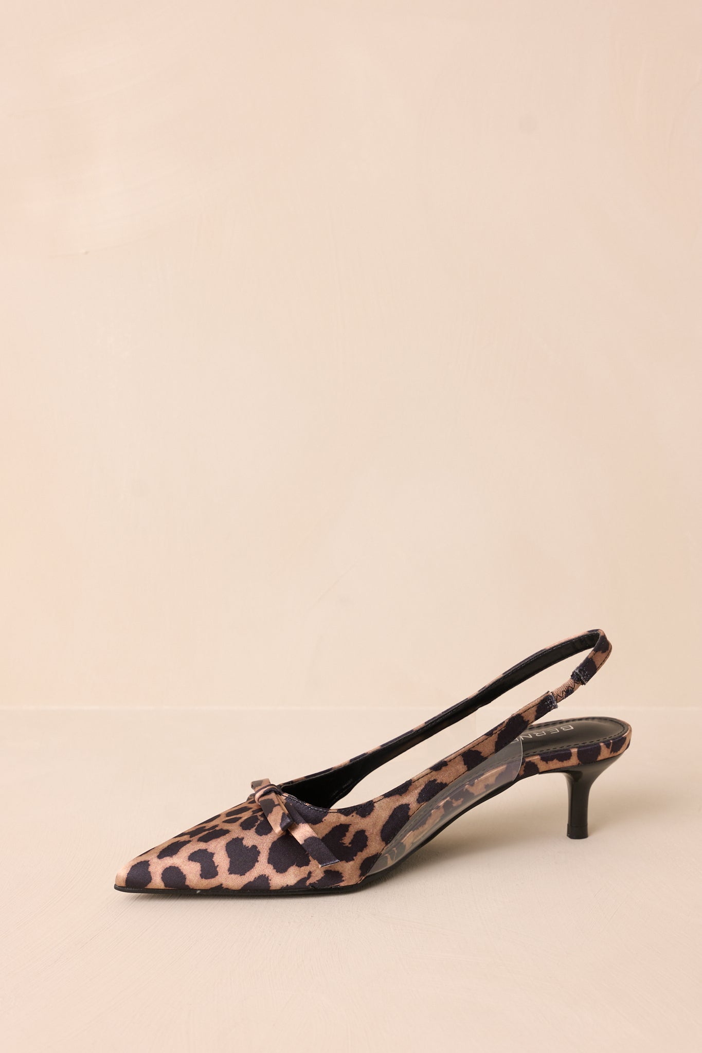 Angled side view of leopard kitten heels highlighting the strap around the back of the foot and the extremely short heel.