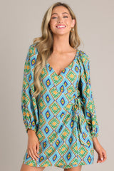 Front view of this turquoise multi print dress that features a wide v-neckline, a self-tie waist feature, elastic shoulders, and elastic cuffed sleeves.
