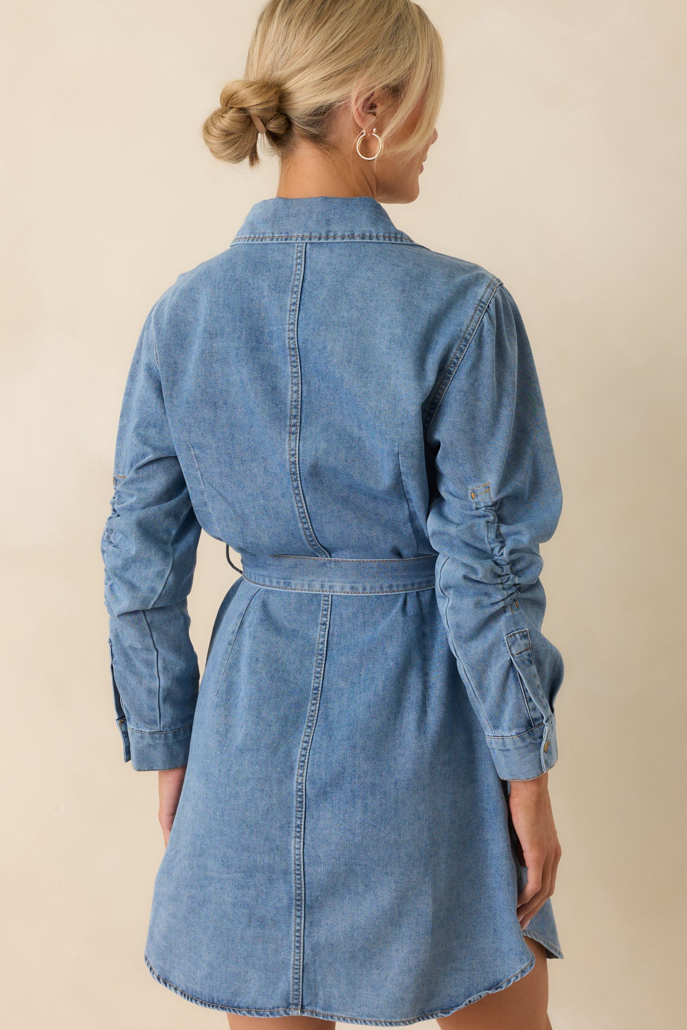 A view from behind of the denim mini dress showing the paneling and belt placement.