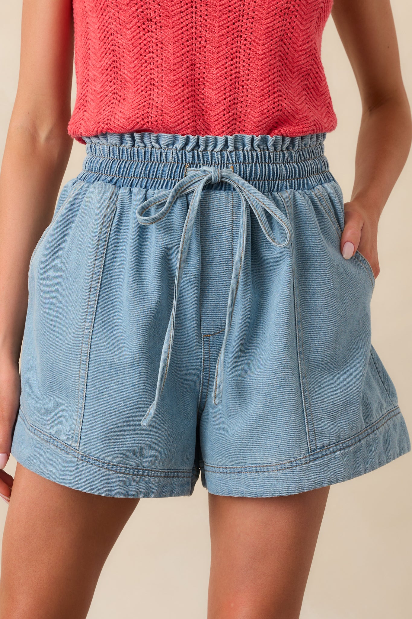 Close-up of the elastic waistband, tan stitching, and ruffle trim on light wash denim shorts