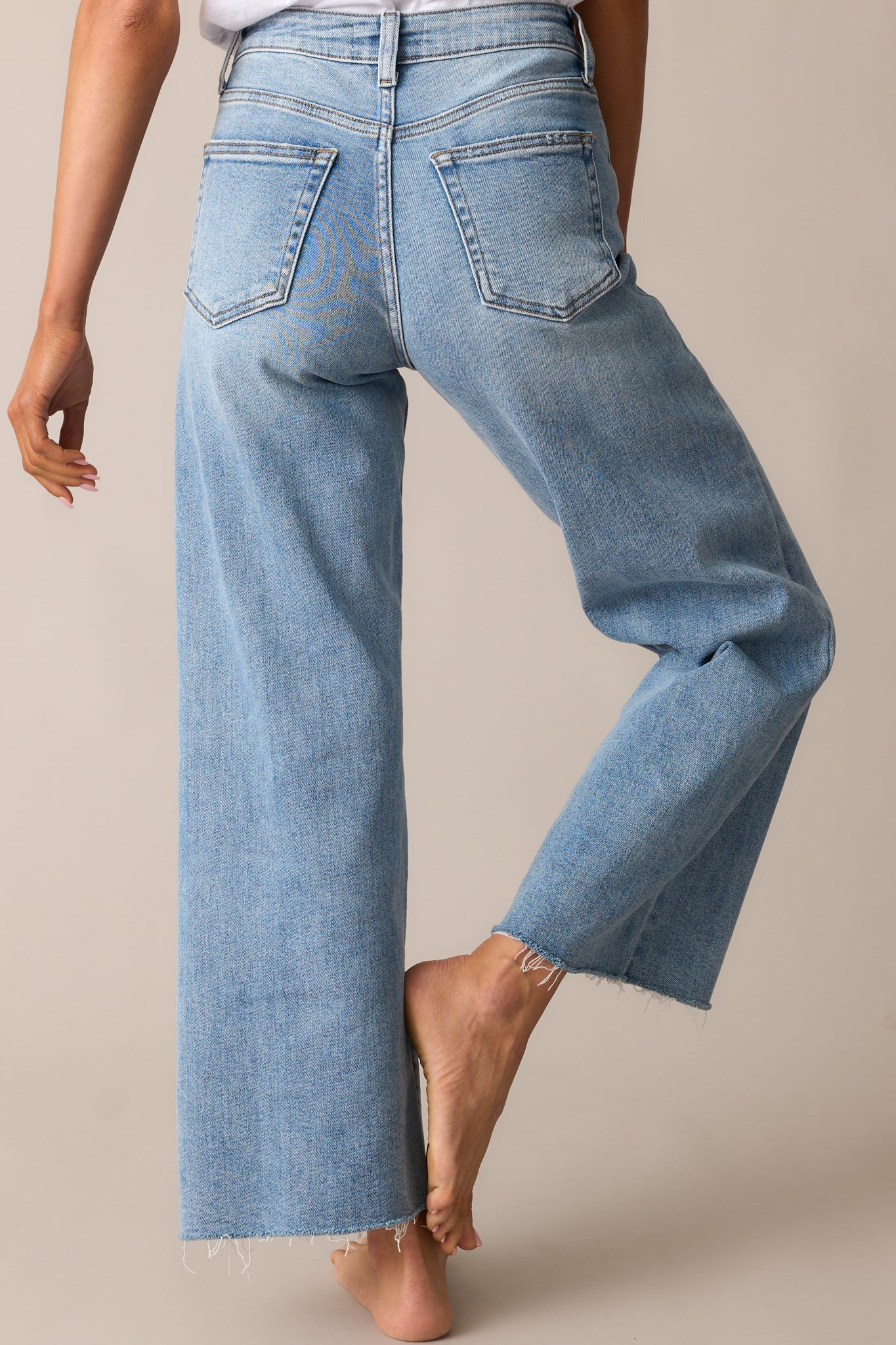 The back of these light wash jeans highlights the functional pockets and wide leg design, with a raw hem completing the look.