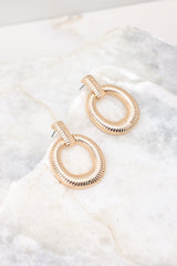Angled overhead view of these gold earrings with rectangular ribbed stud connected to ribbed hoop.