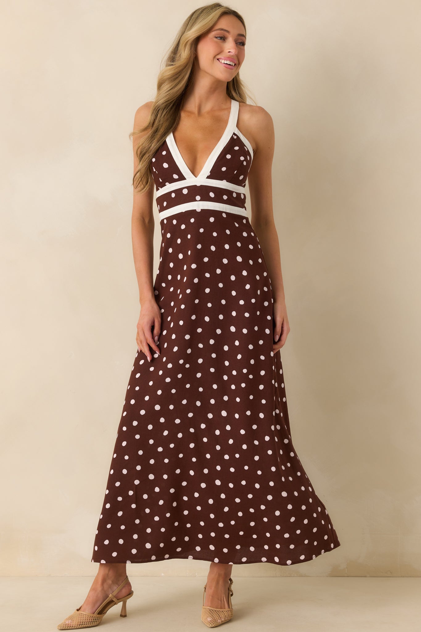 Front view of a chocolate brown maxi dress with ivory polka dot print, deep v-neckline, and white contrast trim.