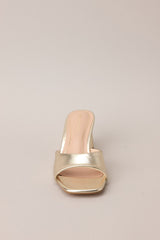Front view of these gold heels with square toe, slip-on design, strap over foot, short circular heel.