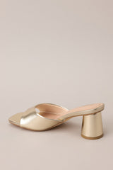 Angled back view of these gold heels with square toe, slip-on design, strap over foot, short circular heel.