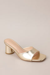 Angled front view of these gold heels with square toe, slip-on design, strap over foot, short circular heel.