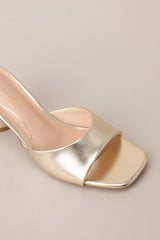 Close up overhead view of these gold heels with square toe, slip-on design, strap over foot, short circular heel.
