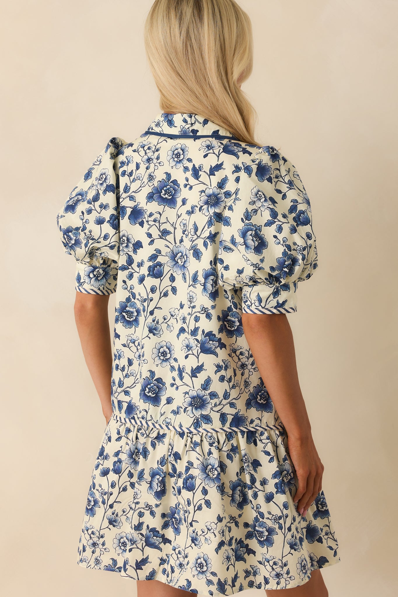 A view from behind showing the navy floral mini dress with cuffed sleeves and a smooth back silhouette.
