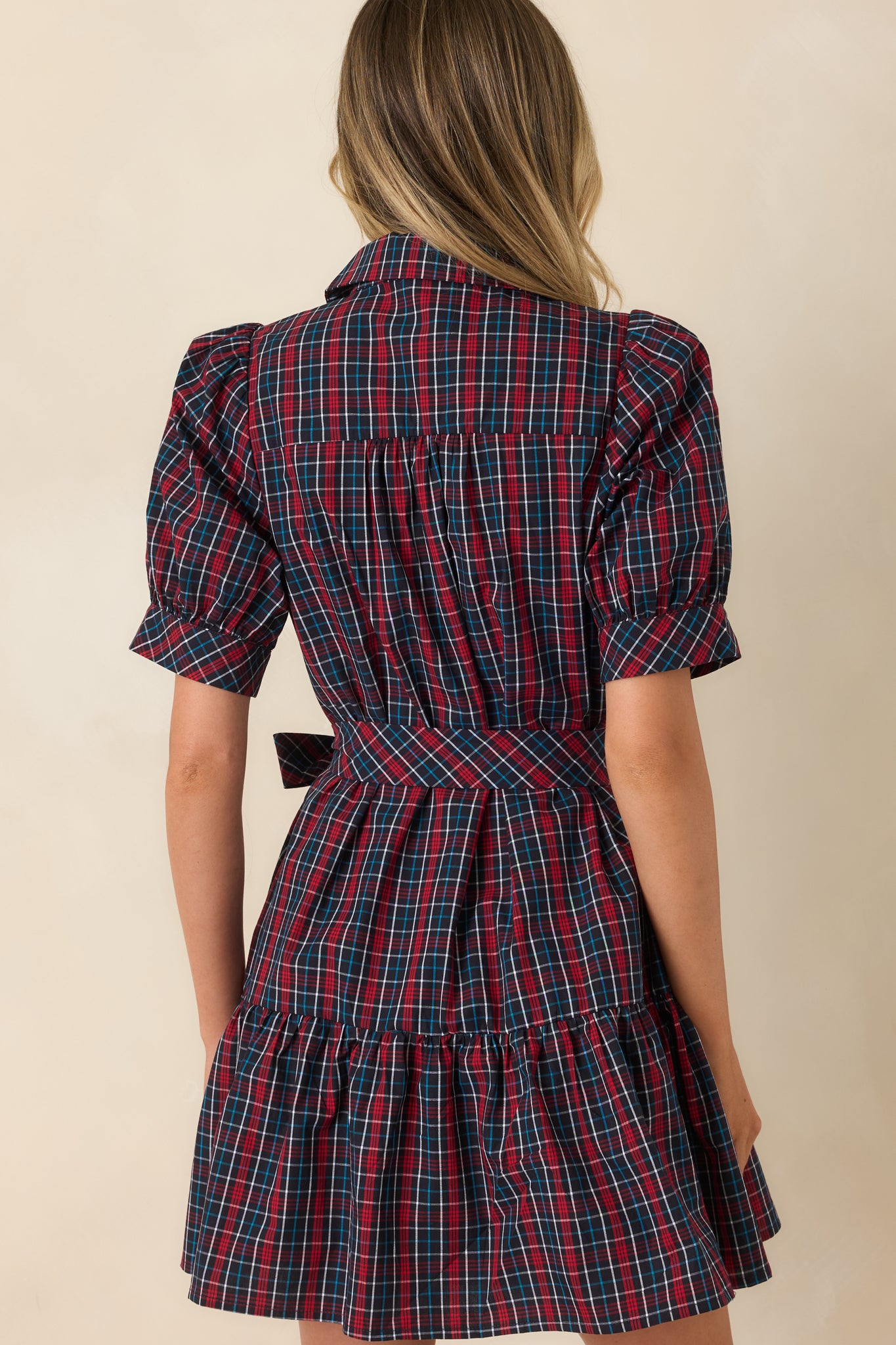 Back view of navy and red plaid cotton mini dress with puff sleeves, belted waist, and tiered skirt.