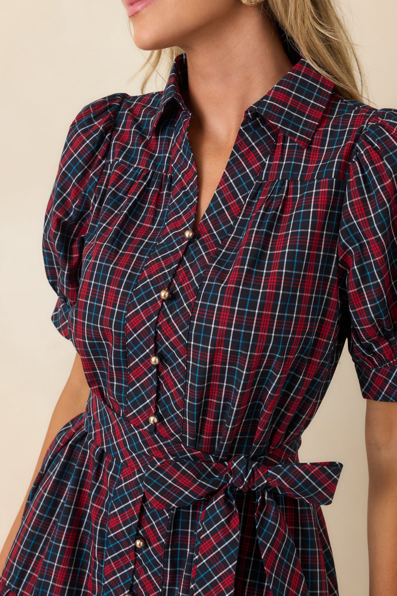 Detail of navy and red plaid mini dress featuring a pointed collar, gold-tone buttons, and plaid waist tie.