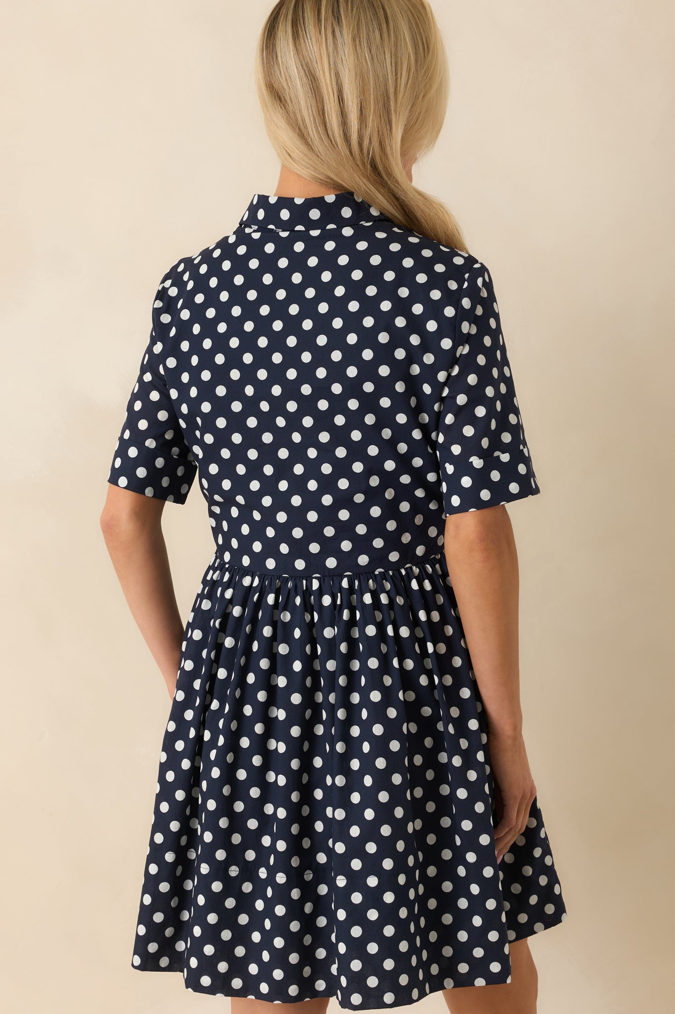  A view from behind of navy mini dress with white polka dots and short sleeves.
