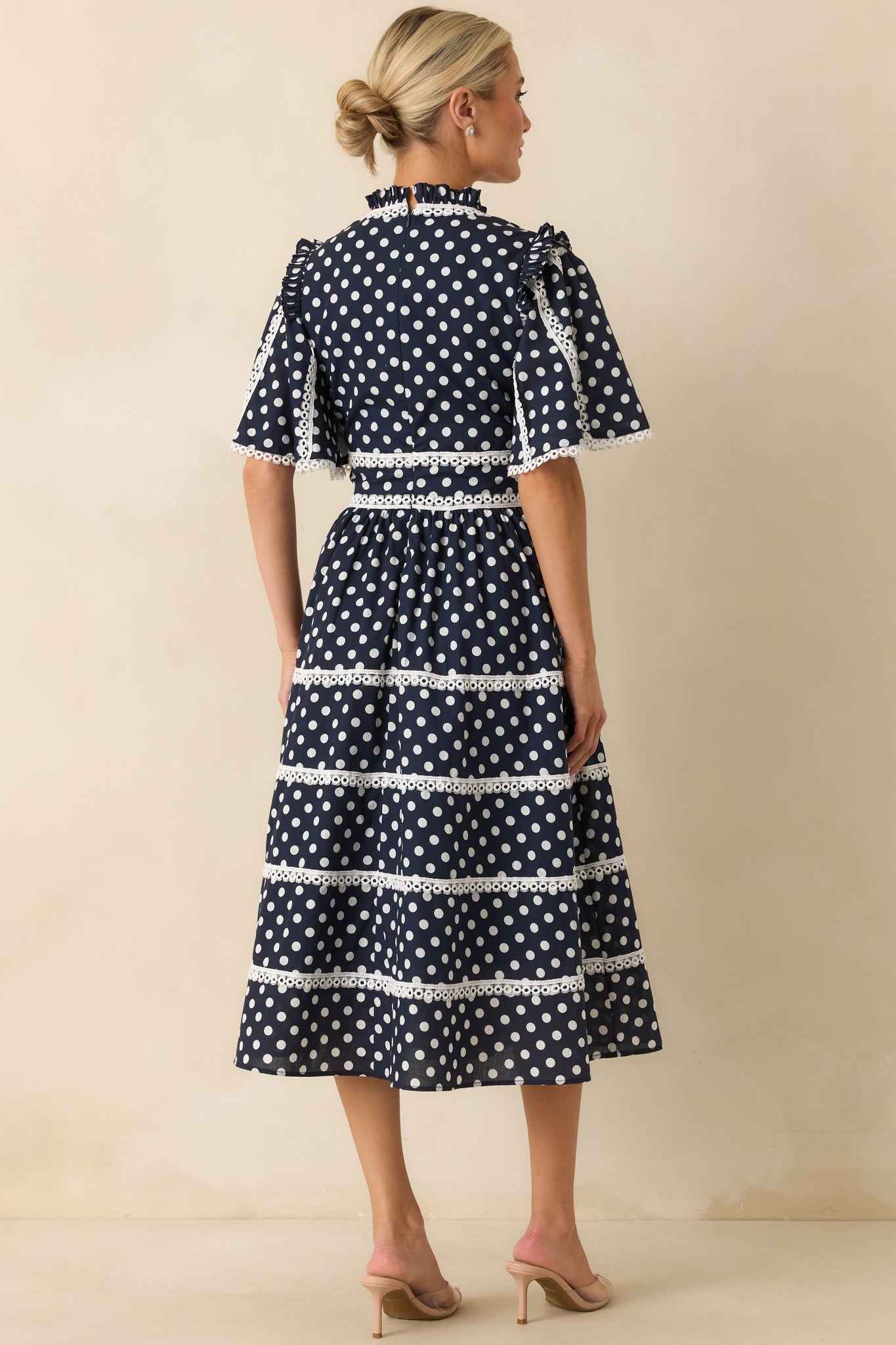  A view from behind of navy midi dress with butterfly sleeves, eyelet trim, and hidden zipper closure.