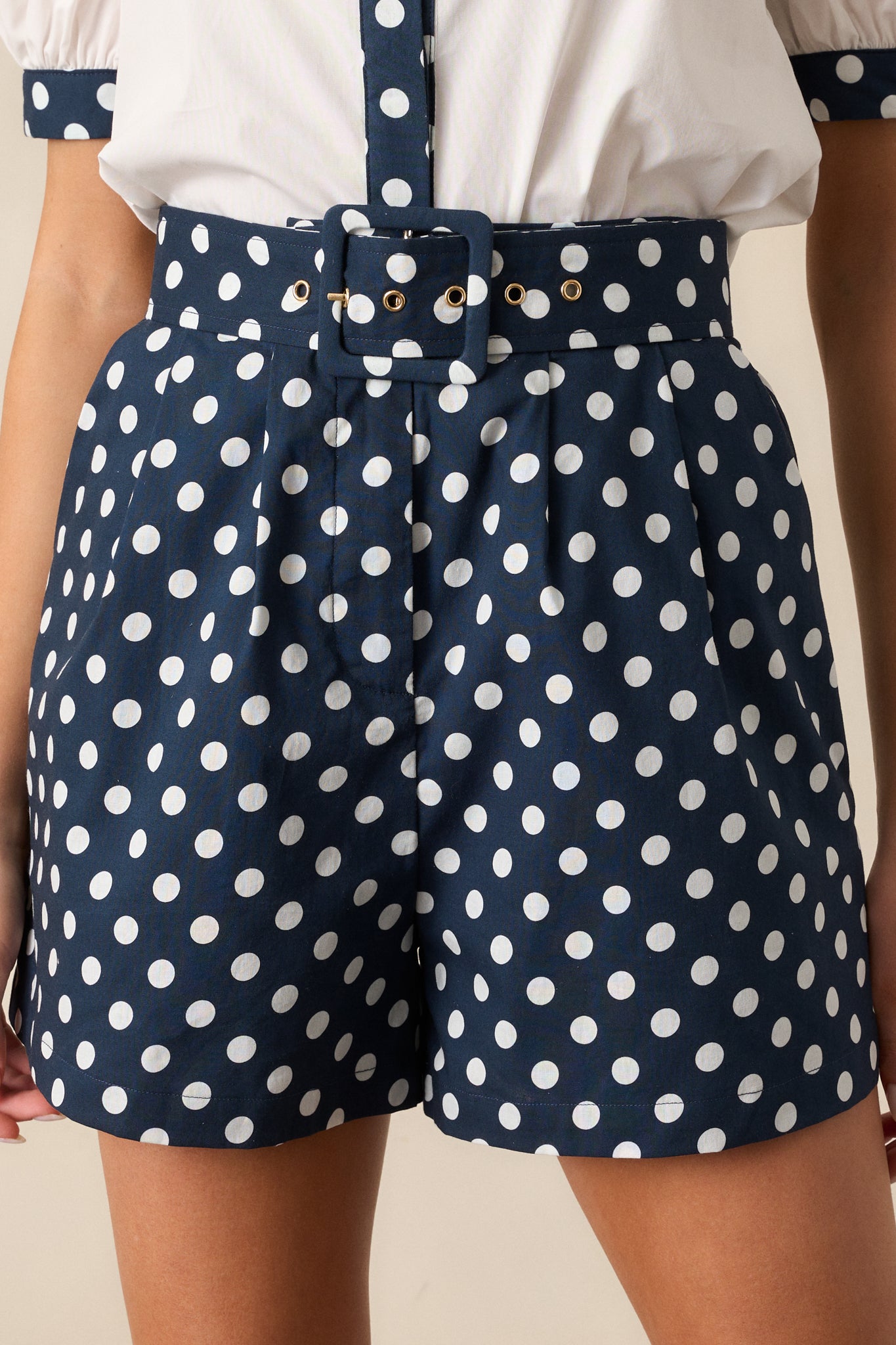 Fabric close-up of navy and white polka dot shorts showing pleats and fine weave.