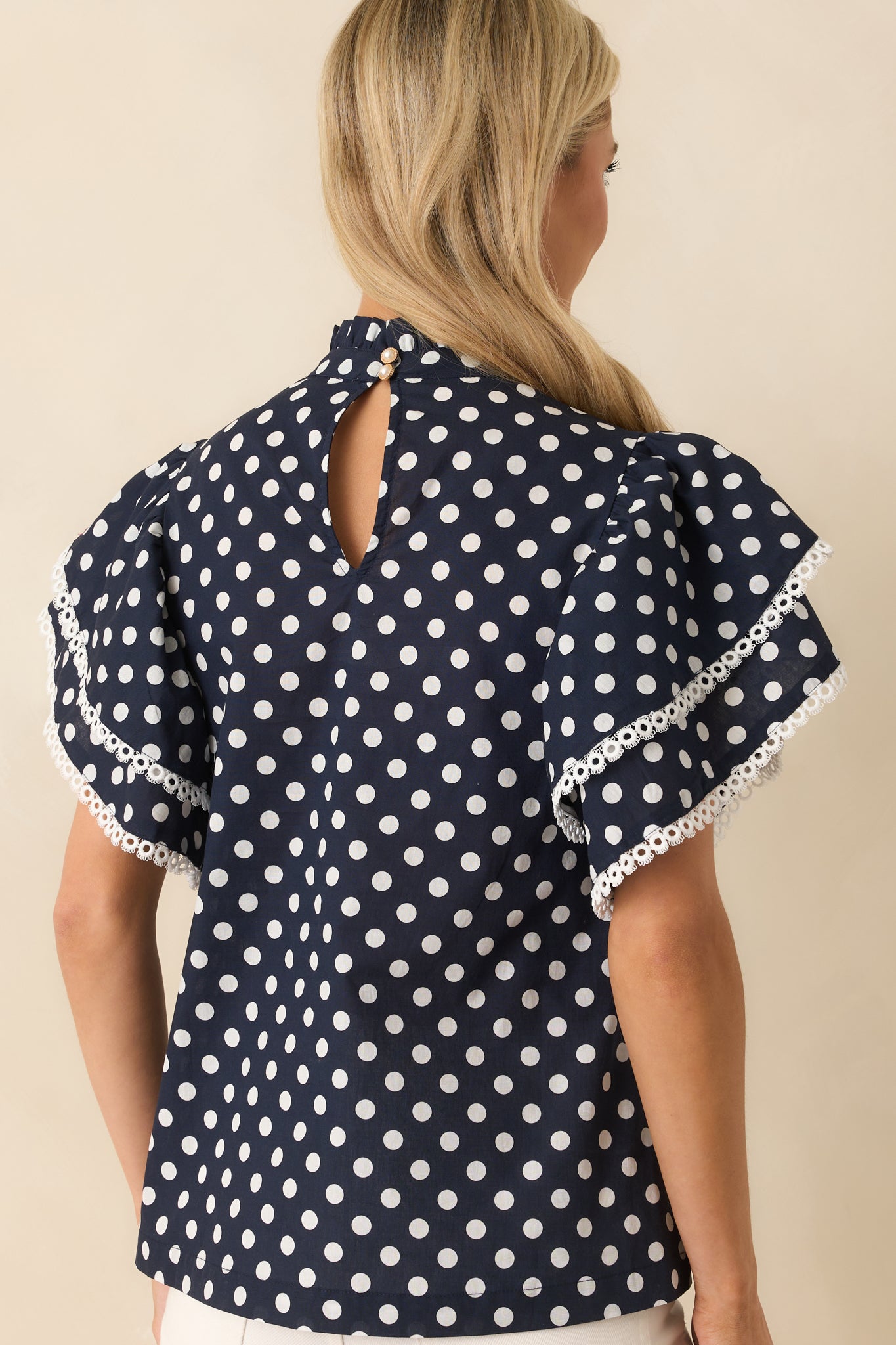 Back view showing the keyhole button closure at the neckline of the navy and white polka dot top with ruffle sleeves.