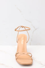 Front view of these light tan heels that feature a thin adjustable ankle strap, straps over the toes, and this heel.