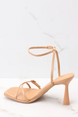 Angled back view of these light tan heels that feature a thin adjustable ankle strap, straps over the toes, and this heel.