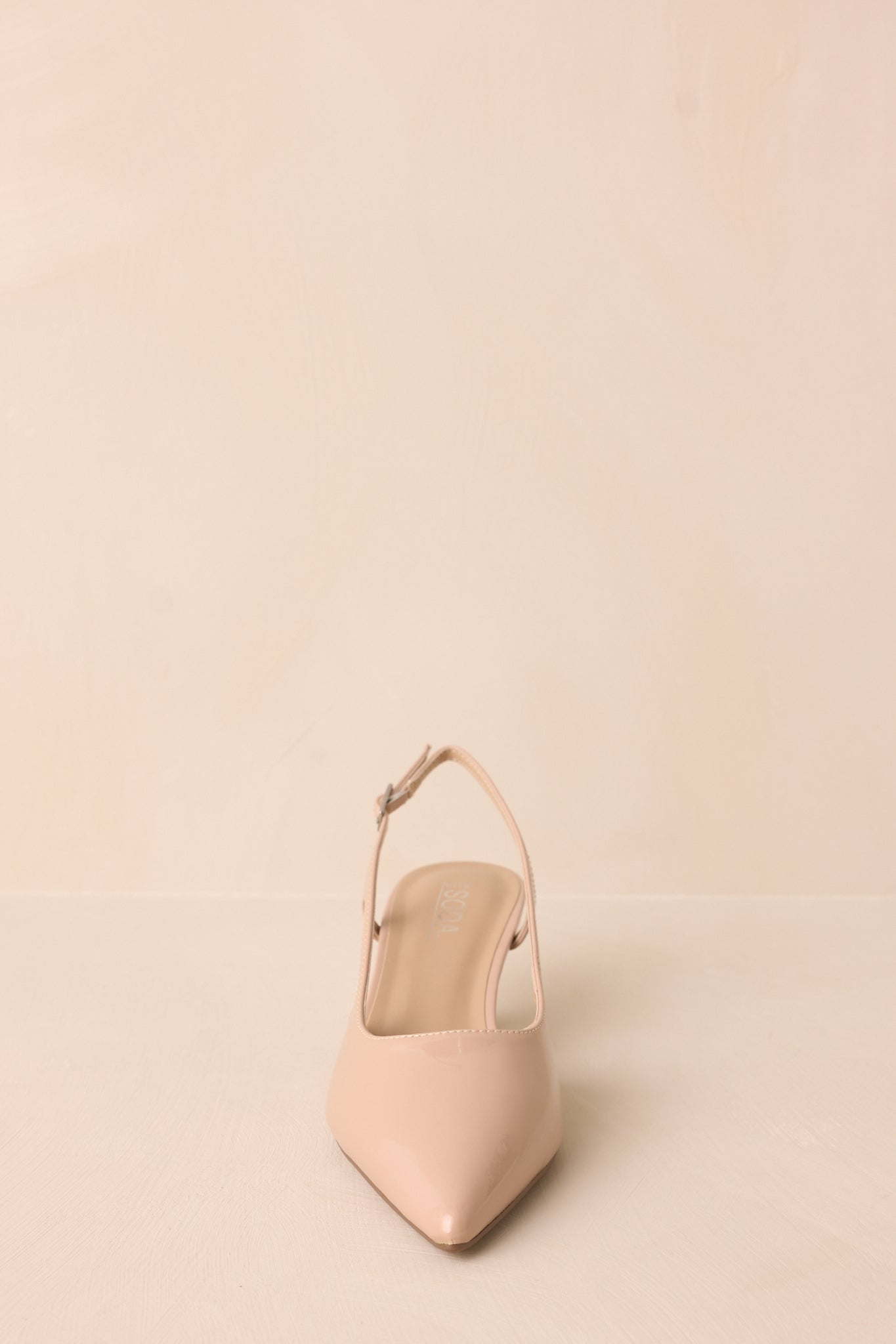 Nude patent pointed heel with gold buckle detail and side cutout, front view.