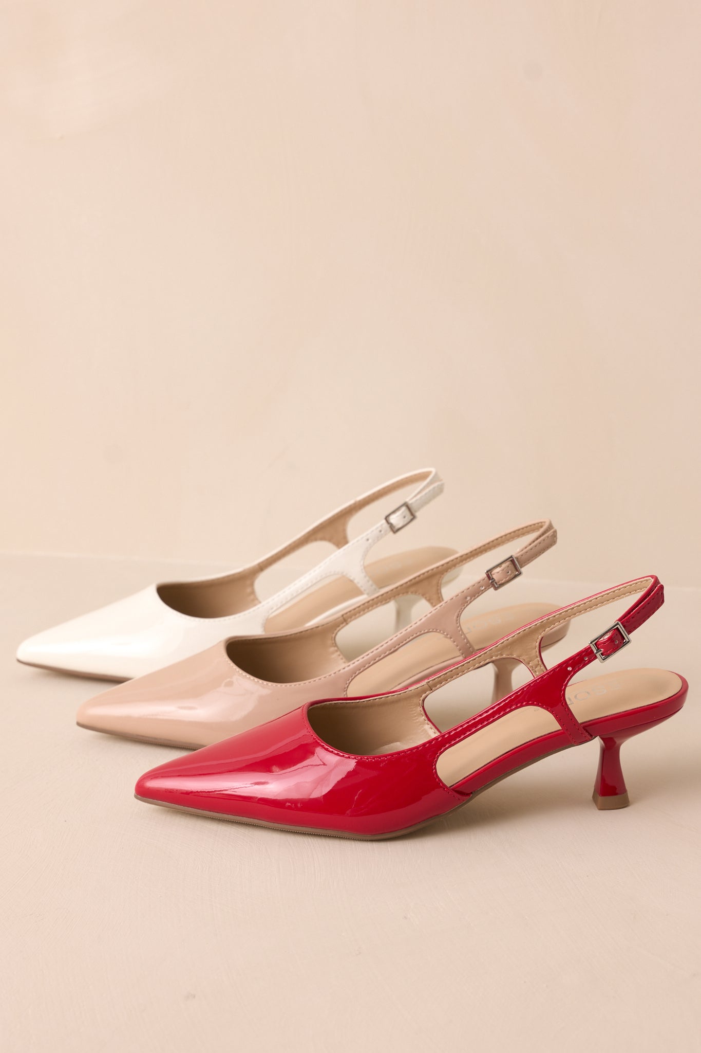 Nude patent pointed heel with gold buckle detail and side cutout displayed with two other color options.