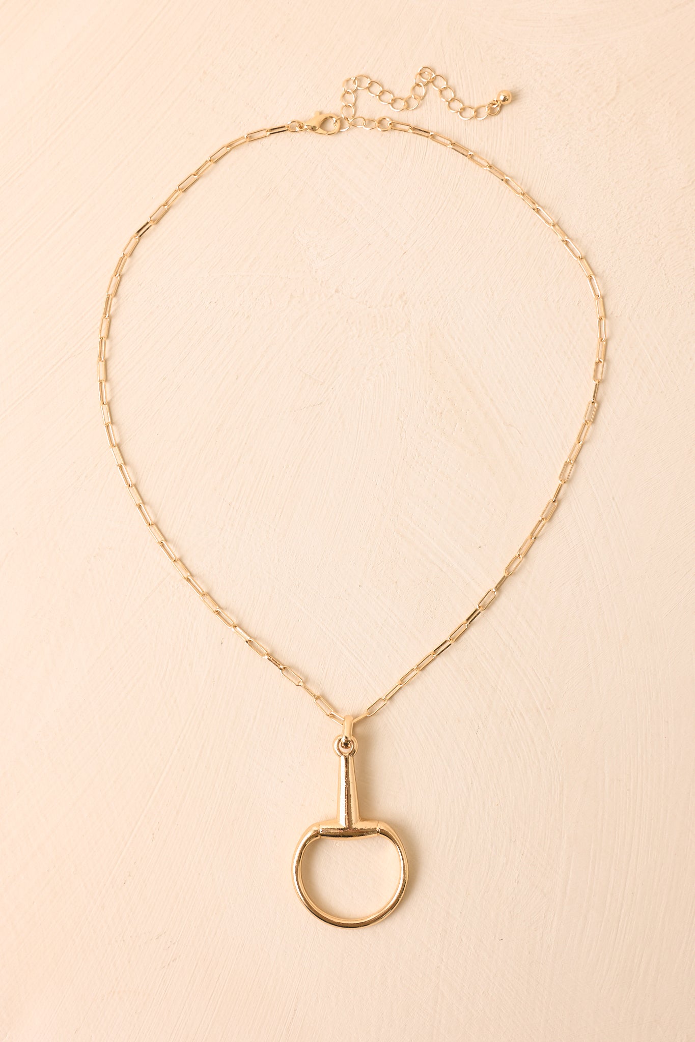 Gold necklace with an equestrian-inspired stirrup pendant on a delicate paperclip chain.