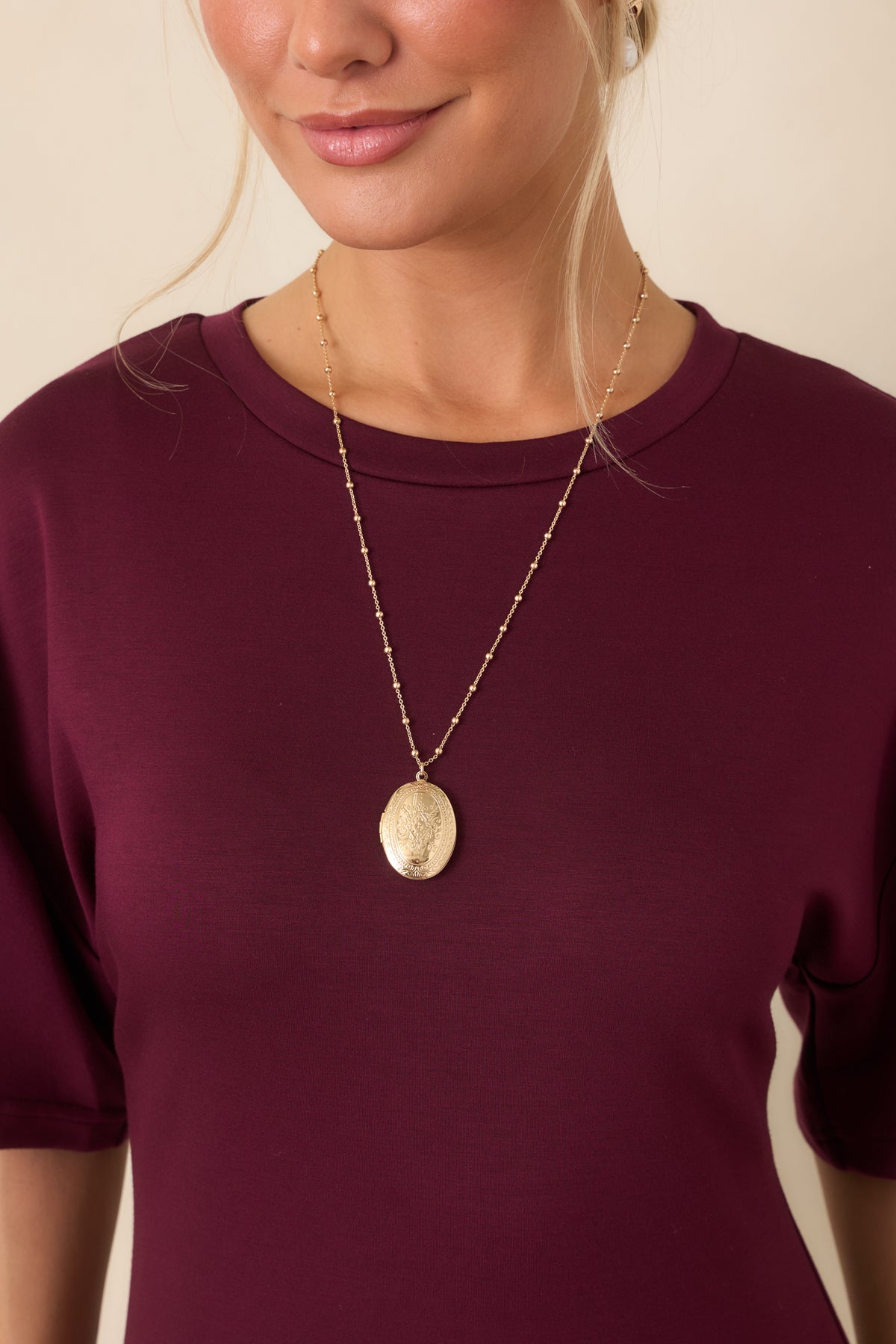 On Repeat Gold Locket Necklace with an oval pendant and delicate beaded chain, worn on a model.