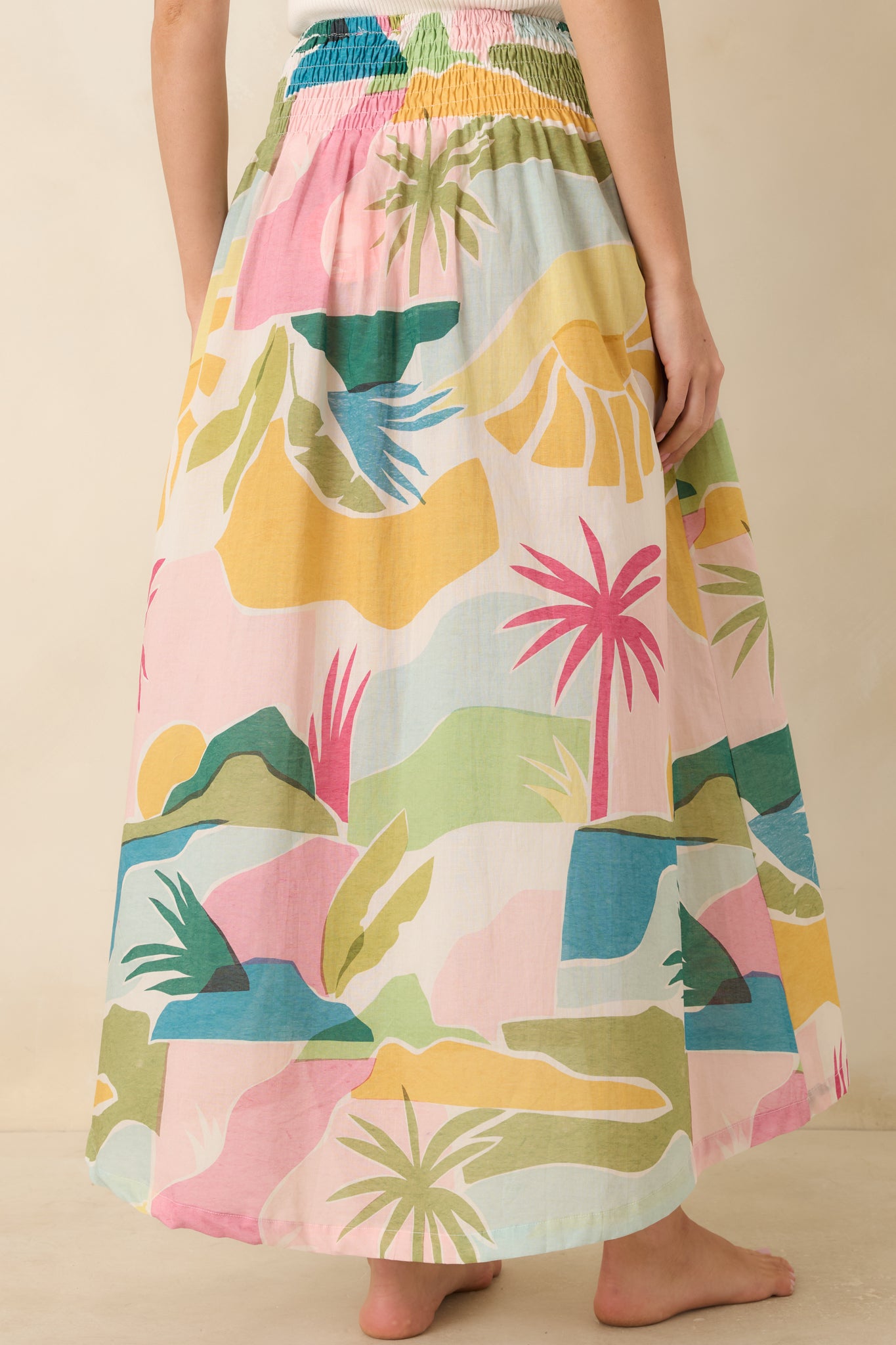Back view of the Paradisa flowy tropical print maxi skirt featuring a smocked elastic waistband and colorful pastel tropical landscape print.