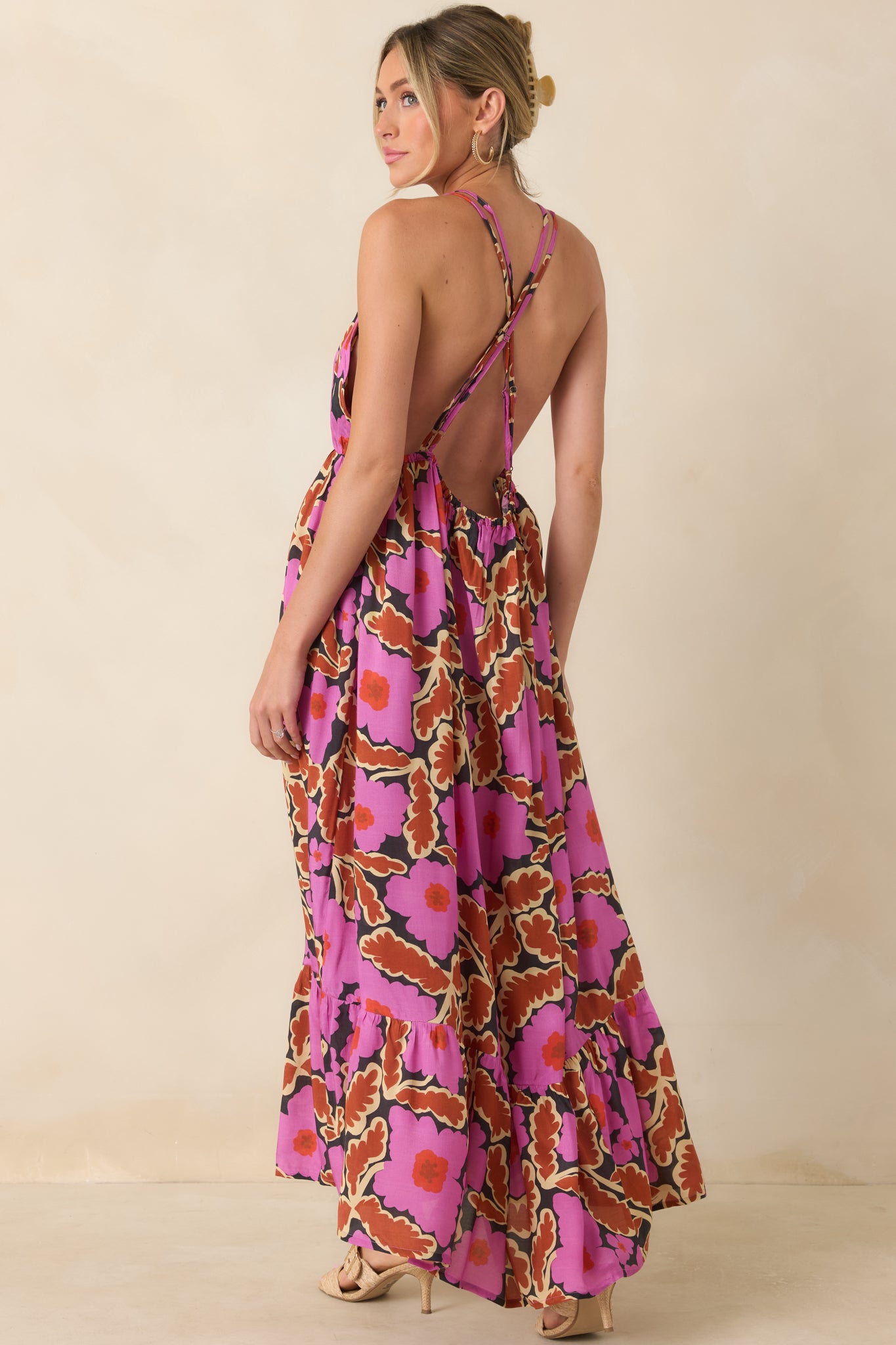 Back view of a pink floral maxi dress featuring a low open back with adjustable crisscross straps and a tiered ruffle hem.