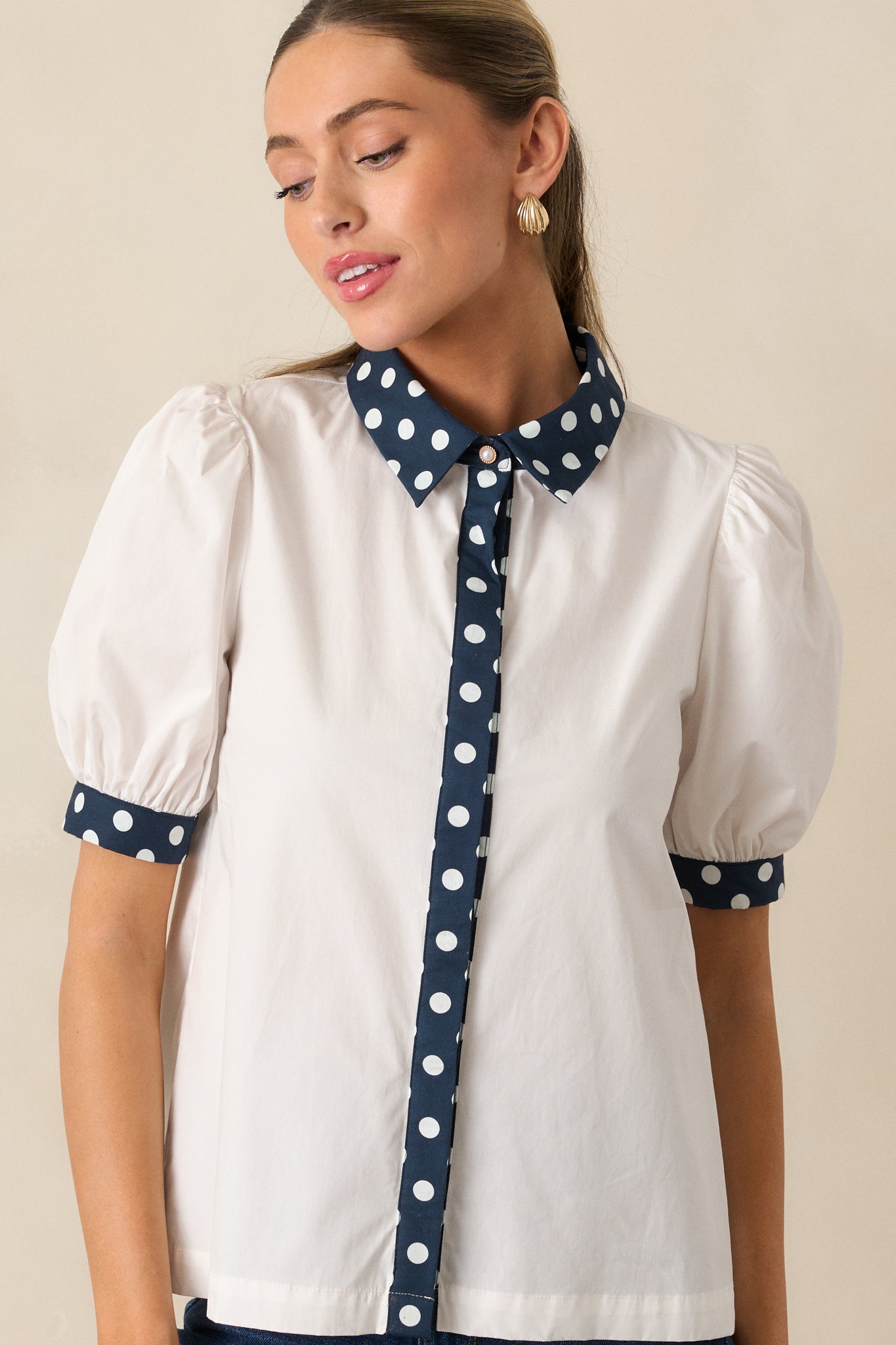 Detail of the cuffed short sleeve and fabric texture of the white top with navy polka dot accents.
