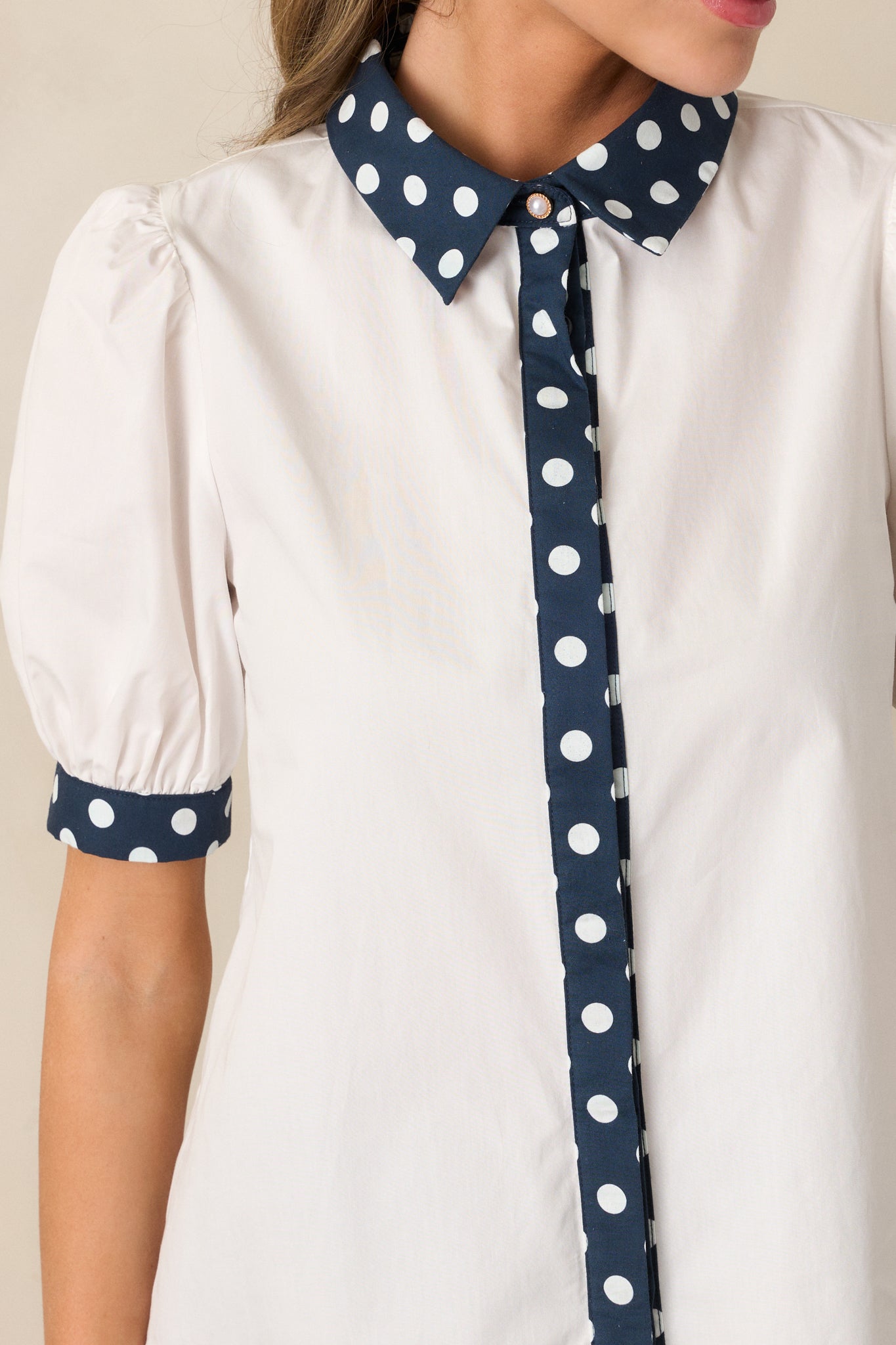Fabric and button detail showcasing the white cotton texture alongside the navy polka dot collar and placket.