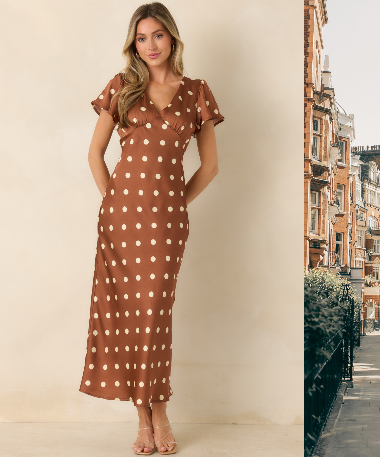 Woman in a satin, brown, polka dot midi dress against a beige background with a scenic London backdrop peeking into the frame. 