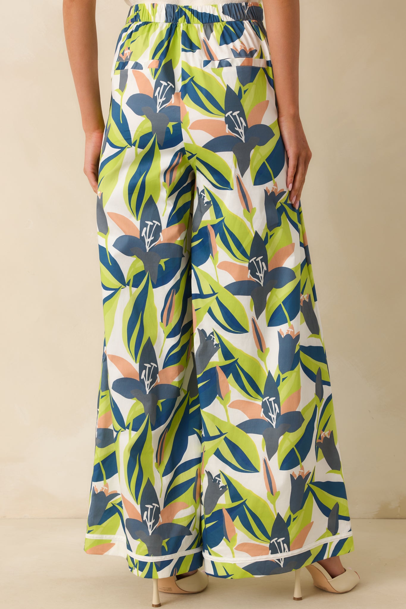 Back view of wide-leg pants featuring elastic back waist insert, faux slit pockets, and full floral print.