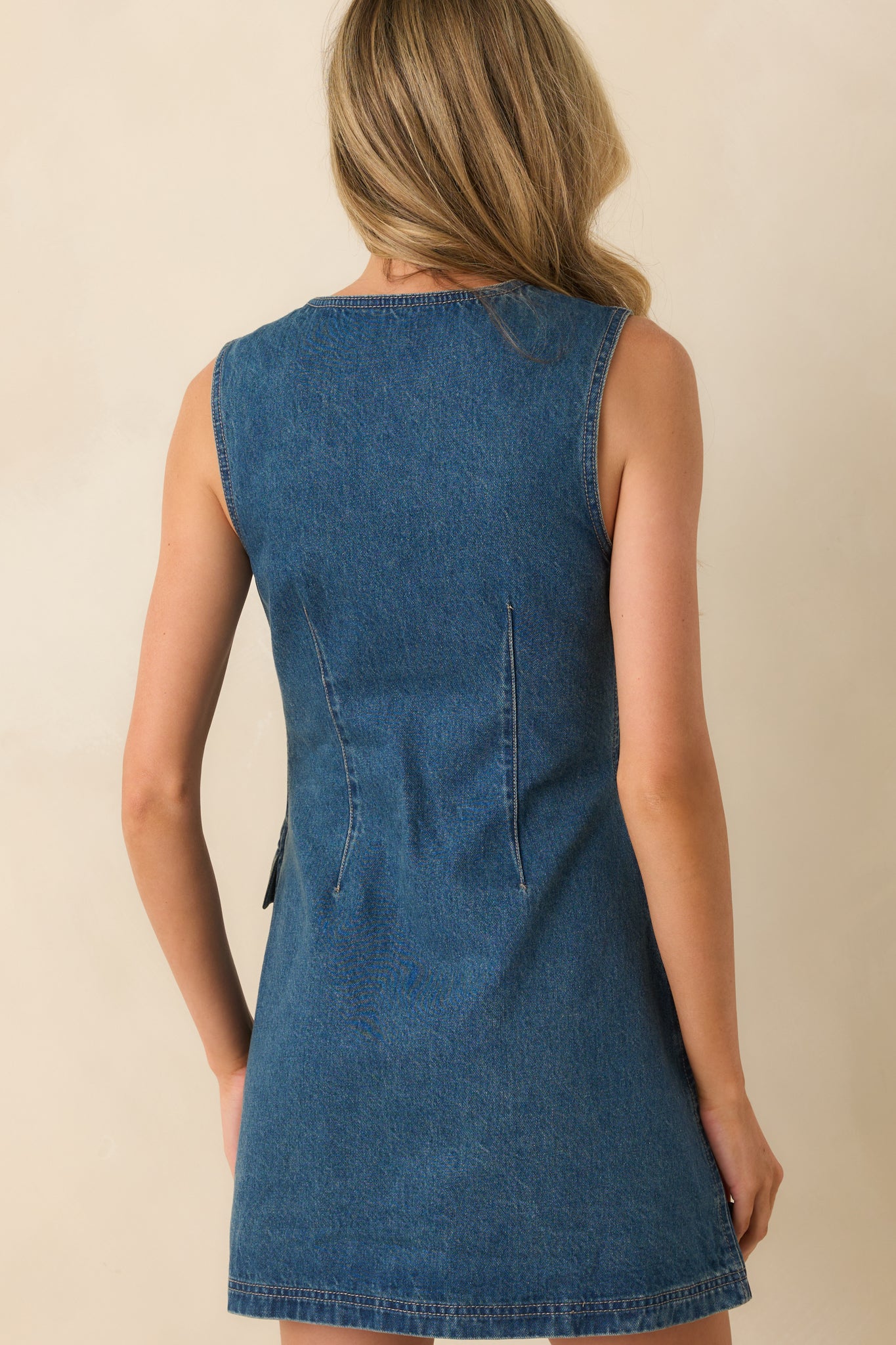 Rear view of medium wash denim mini dress with sleeveless cut and panelled design.