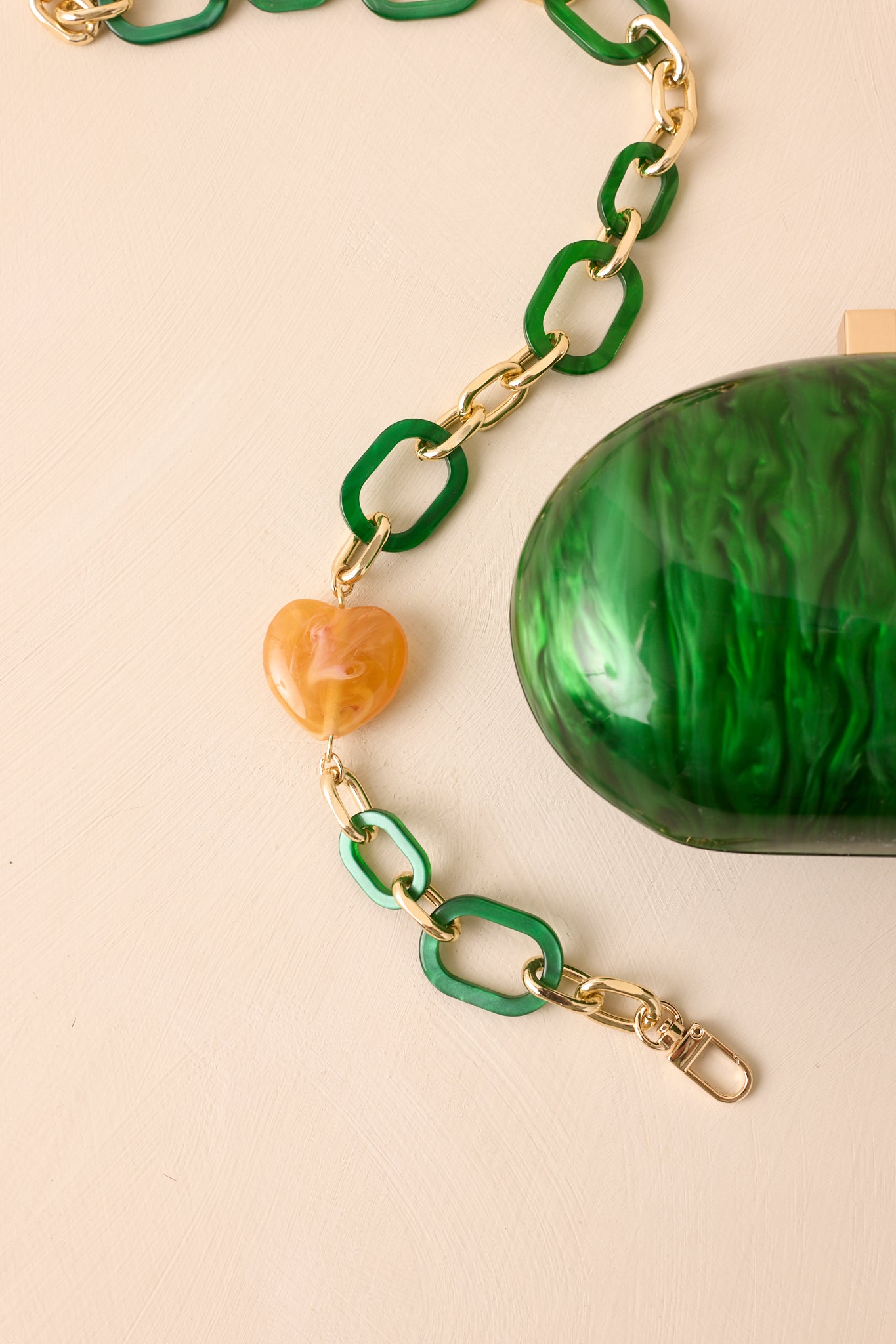 Detailed shot of the resin-and-gold shoulder strap with an amber bead, paired with the glossy emerald clutch.