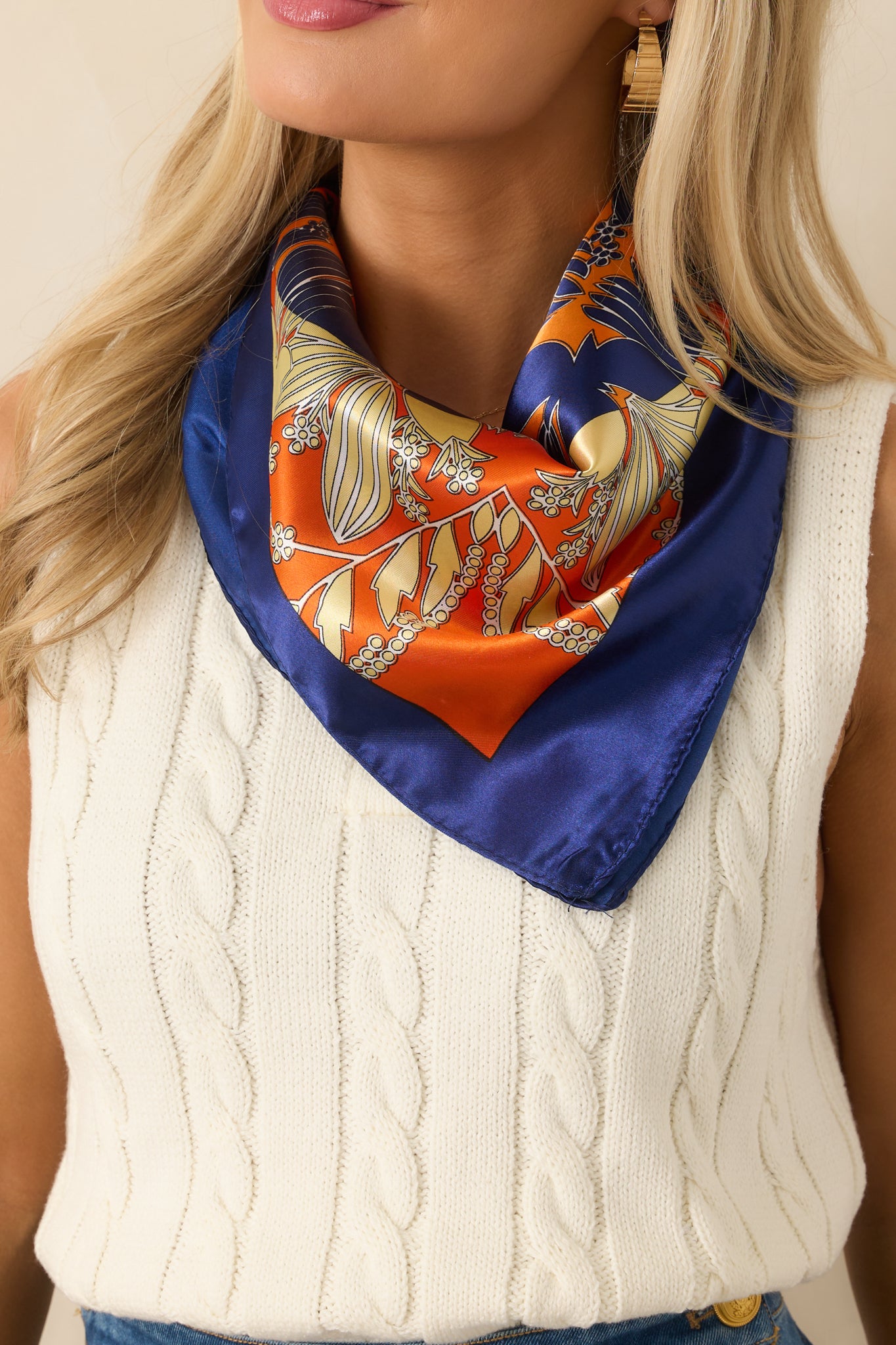 Satin orange scarf featuring a contrast border and bold geometric floral design, draped elegantly around the neck.
