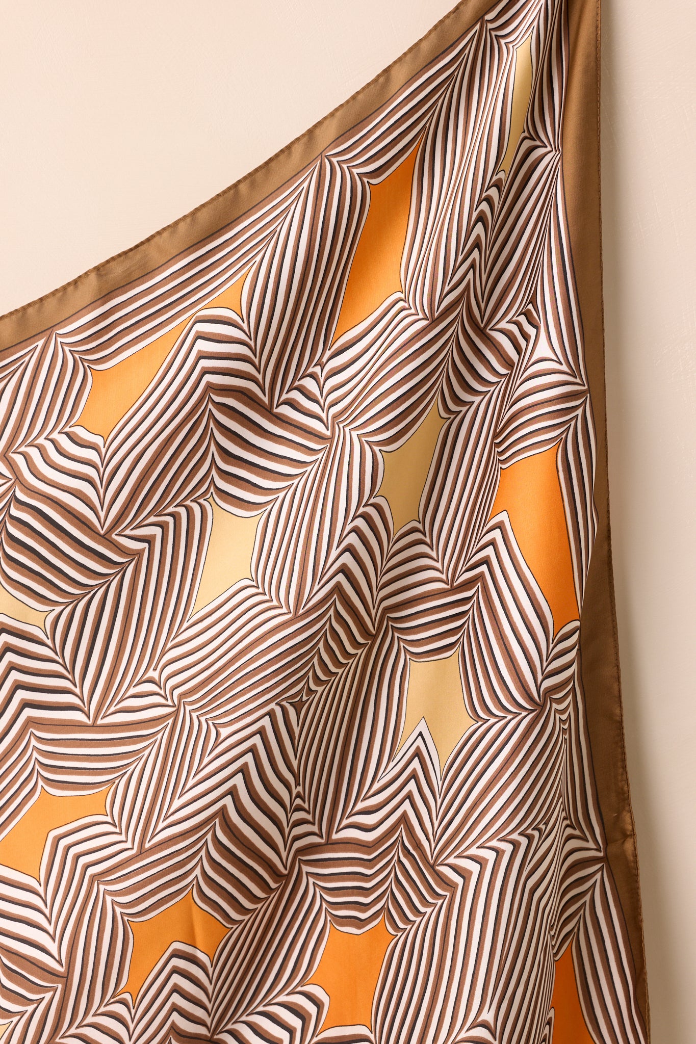 Close-up of the scarf showing intricate stripe patterns with orange and golden yellow highlights on the brown satin material.