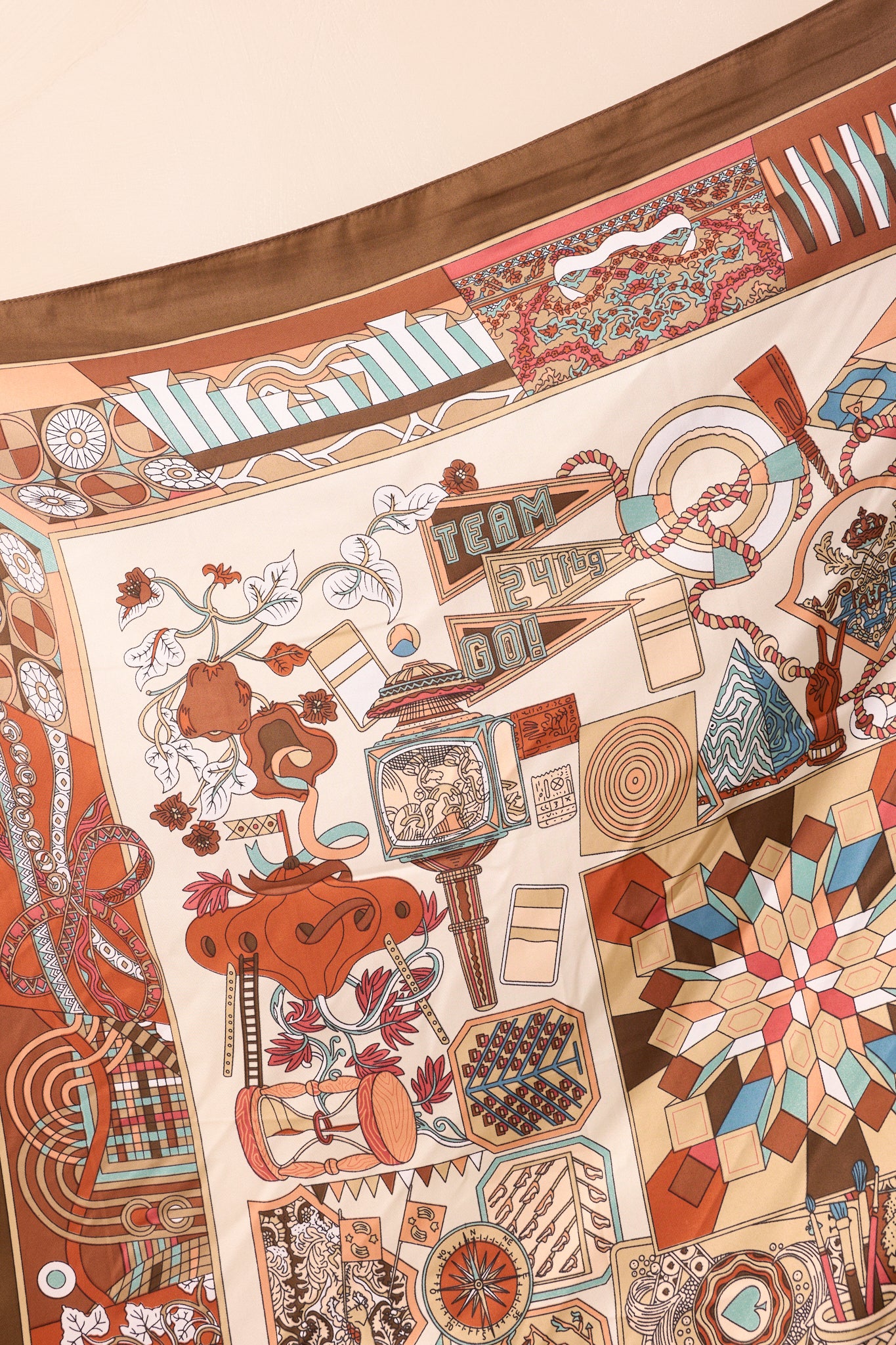 Close-up of one corner of the scarf showcasing intricate multicolor motifs against the brown background with a glossy satin texture.