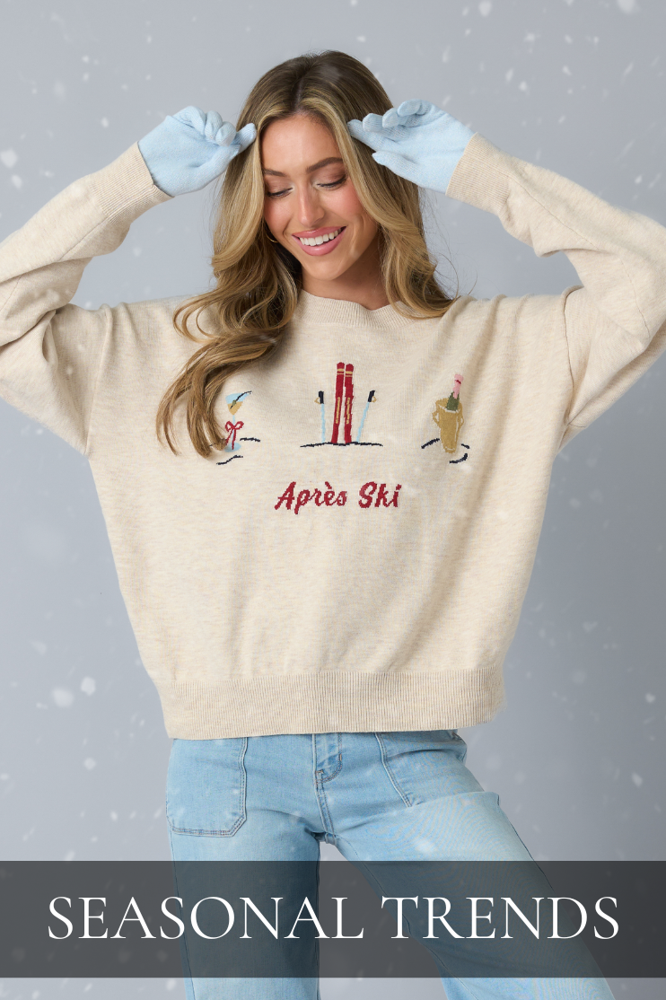 Woman wearing a cream sweater with Après Ski embroidery and light denim, linking to the Seasonal Trends shop.