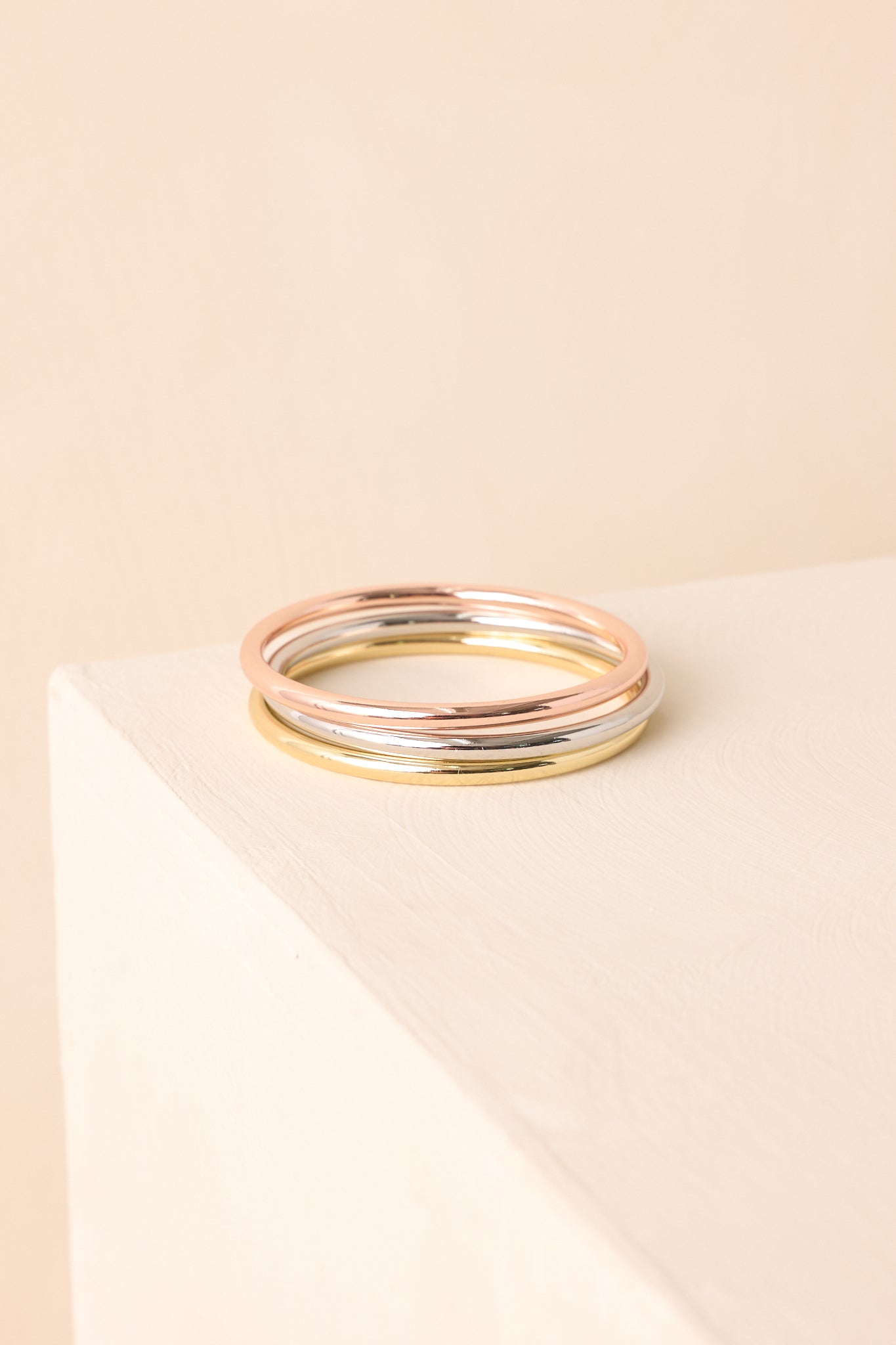 A set of three polished slip-on metal-tone bangles arranged against beige backdrop.