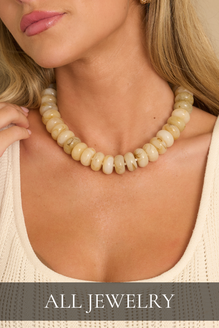 Shop all jewelry featuring a chunky cream stone beaded statement necklace styled with a cream knit sweater.