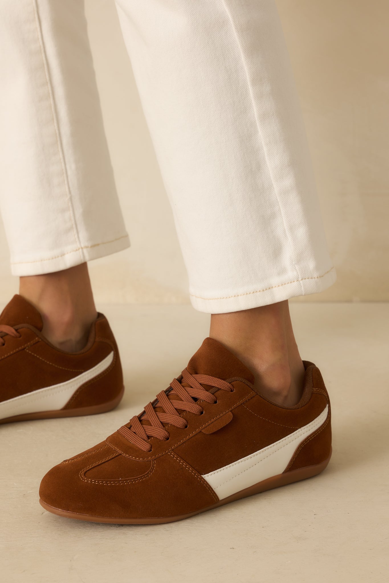 A side angle of the brown faux suede sneakers with white faux leather detail, lace-up front, and cushioned sole.