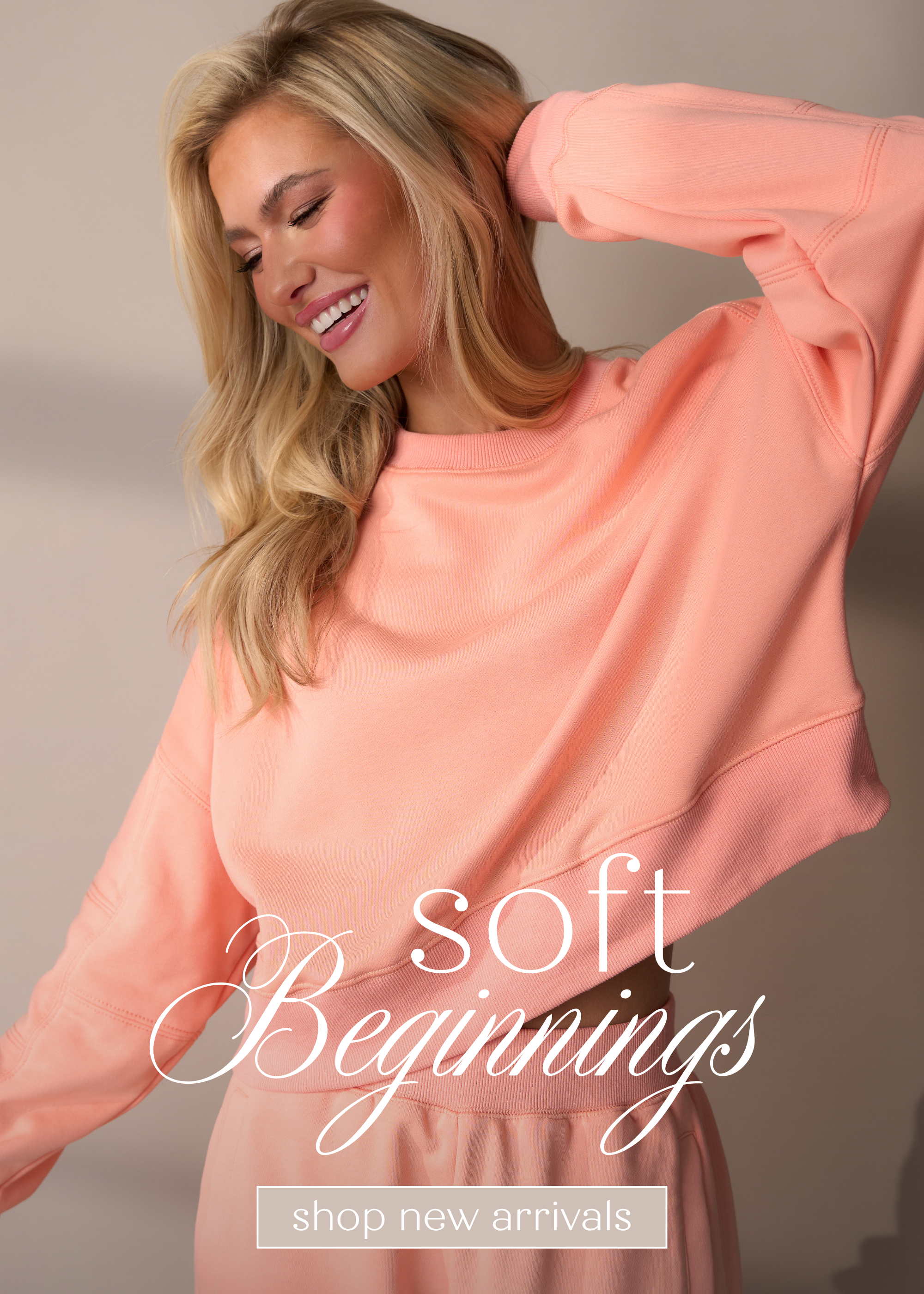 Woman smiling in a peach cropped sweatshirt and matching lounge pants from the Soft Beginnings collection. Shop these new styles.