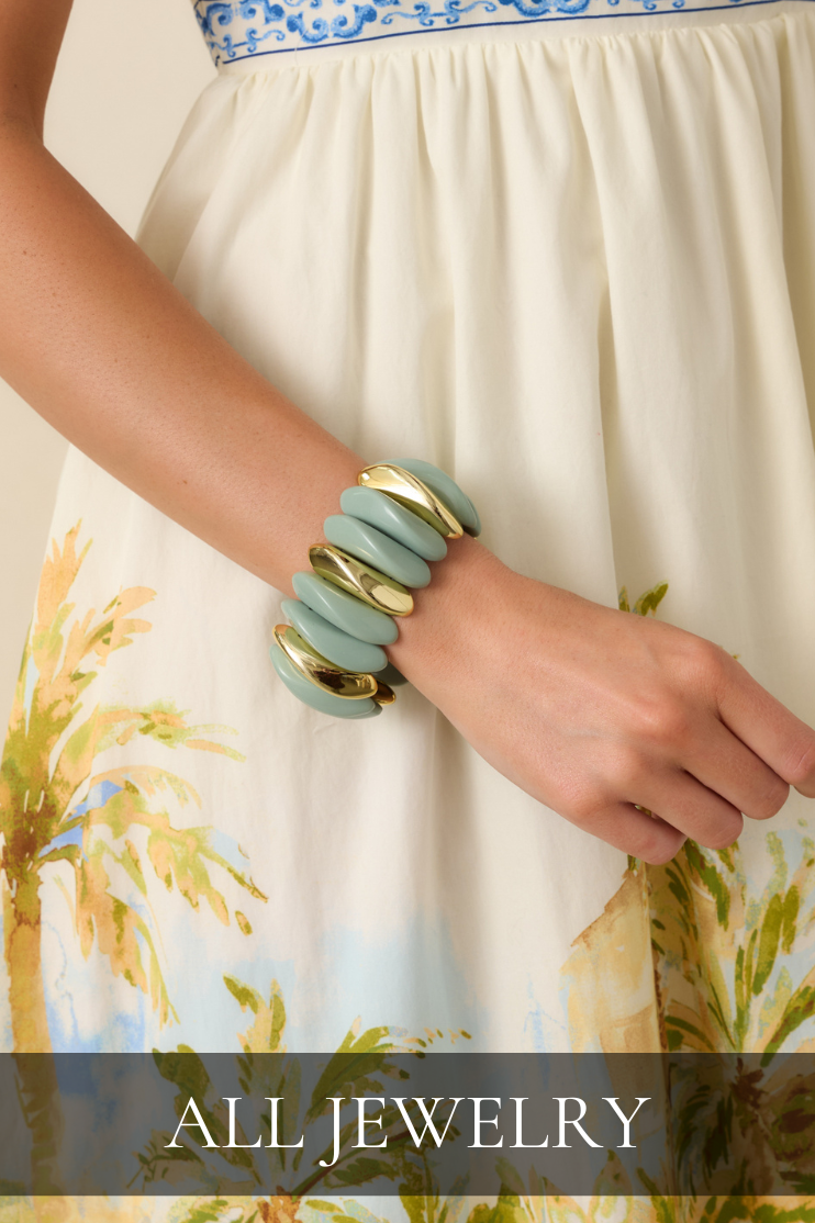 Stacked mint resin and gold bangle bracelet worn with a tropical print dress representing the women’s jewelry collection.