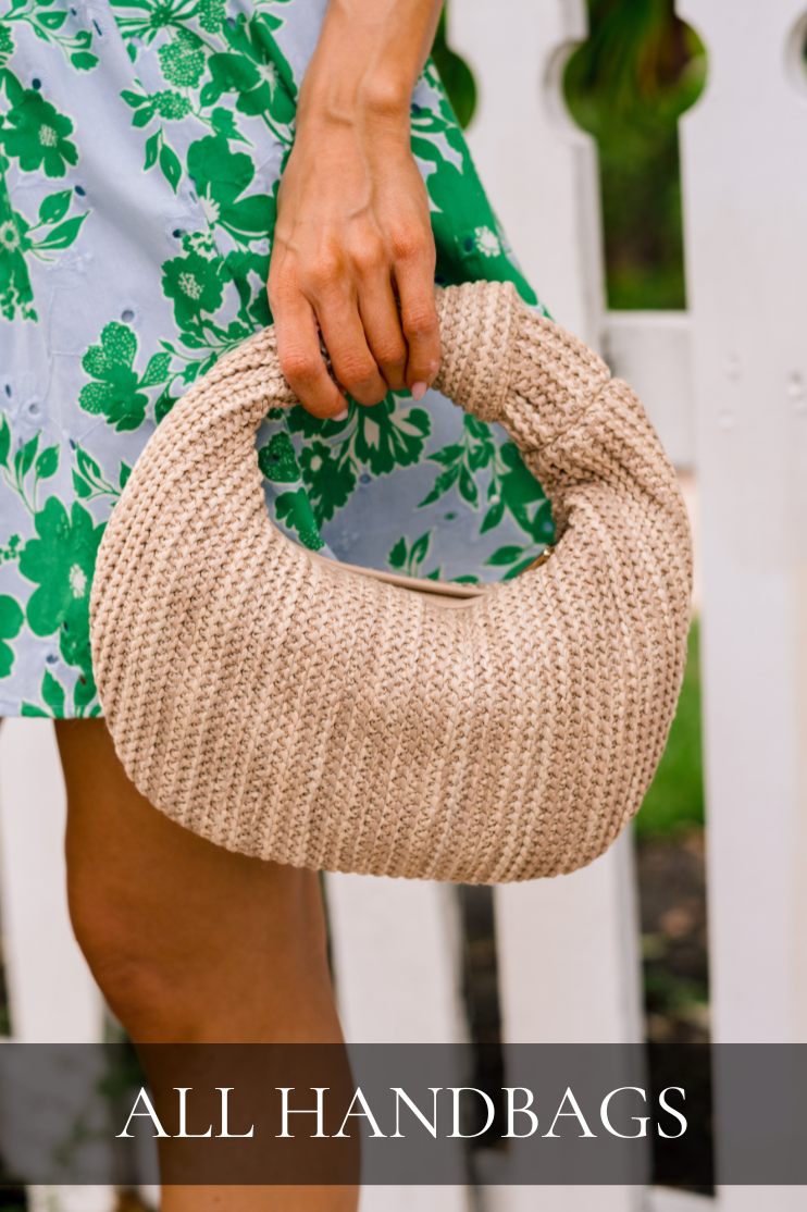 Model holding a woven beige handbag in front of a white fence, styled with a green and blue floral dress. Bag is featured in All Handbags collection.