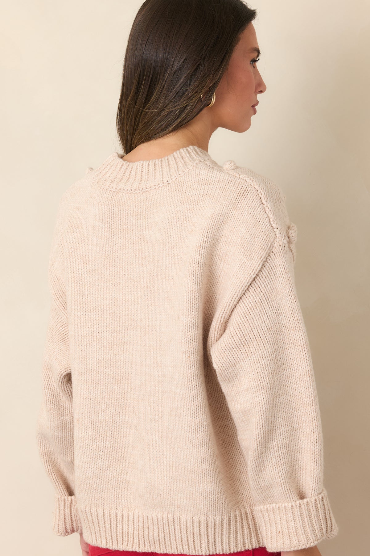 Back view of the beige cherry bobble knit sweater showing its plain knit back, dropped shoulders, and ribbed trim.