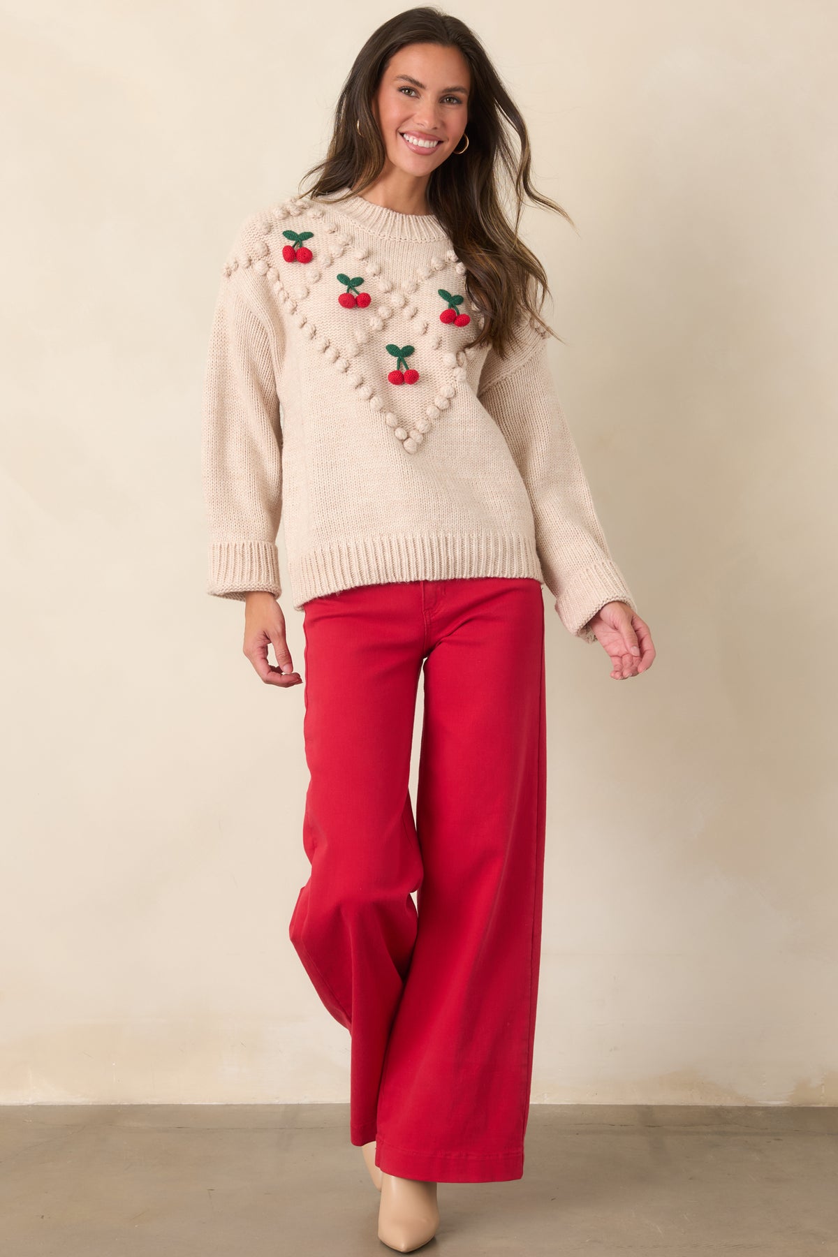 Model walking in a beige cherry bobble knit sweater, showing its relaxed drape, long sleeves, and ribbed hem.