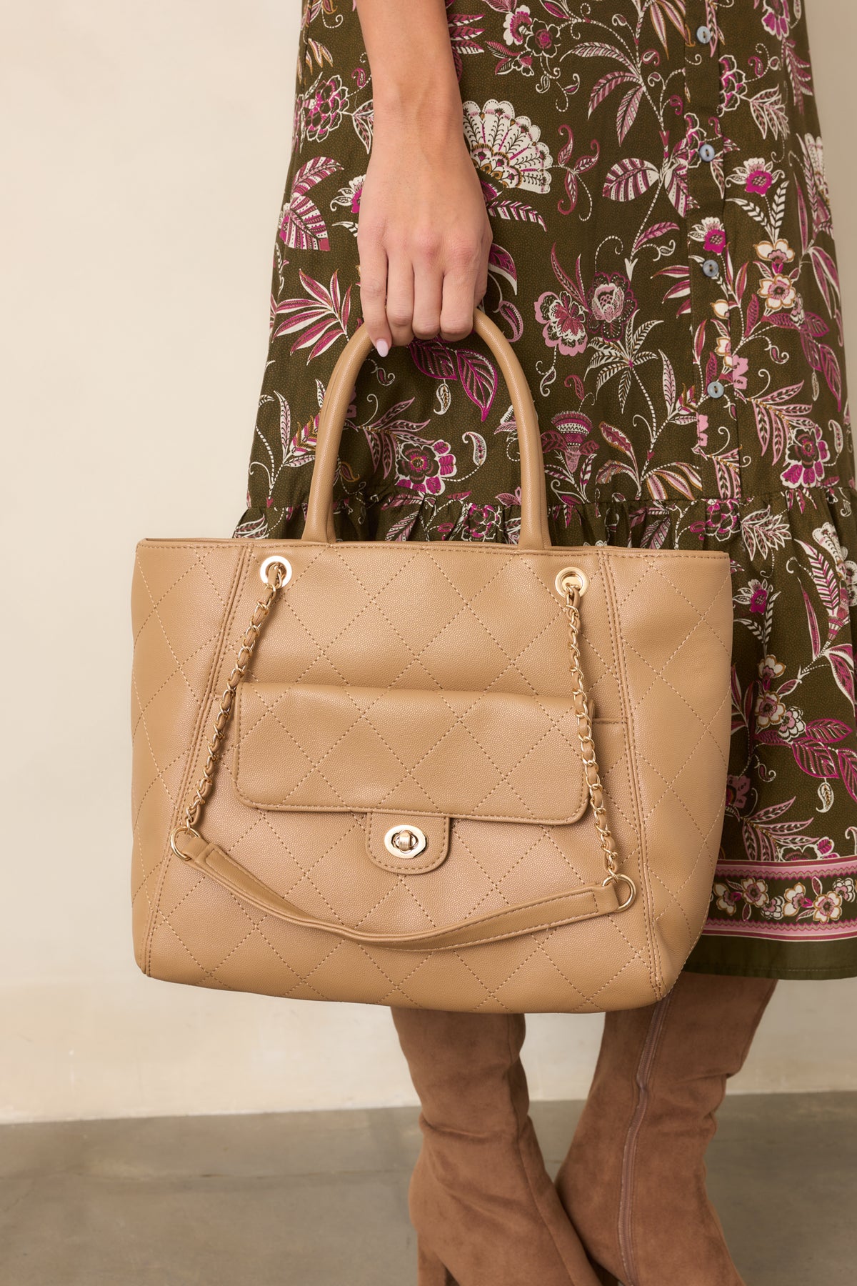 Woman carrying a tan quilted tote bag with gold chain detailing styled with a floral fall dress and brown boots.