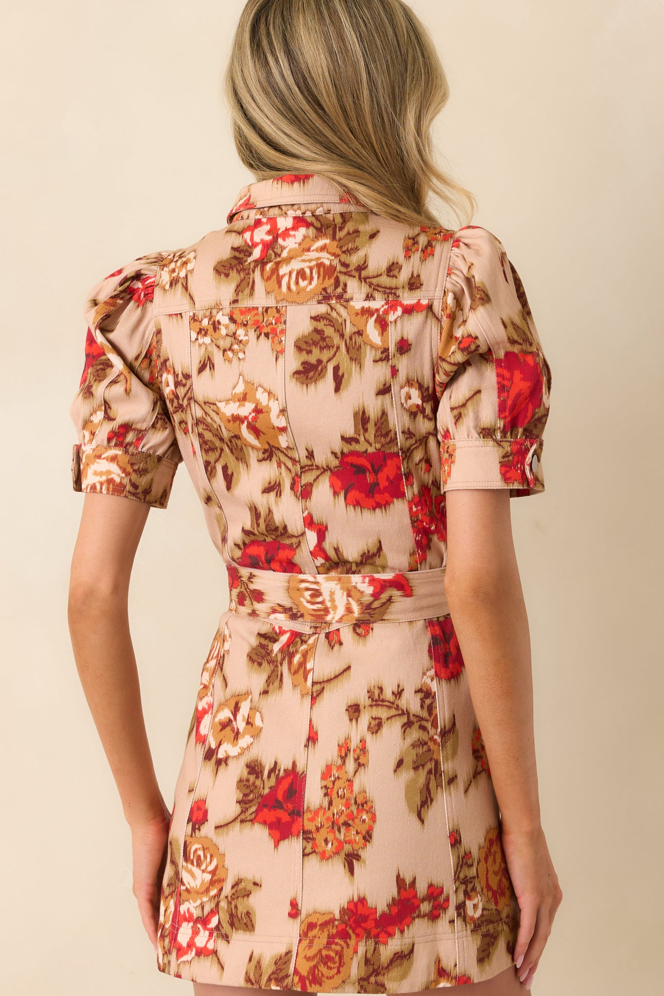 A view from behind of tan mini dress showing short puff sleeves, paneled design, and optional self-tie belt.