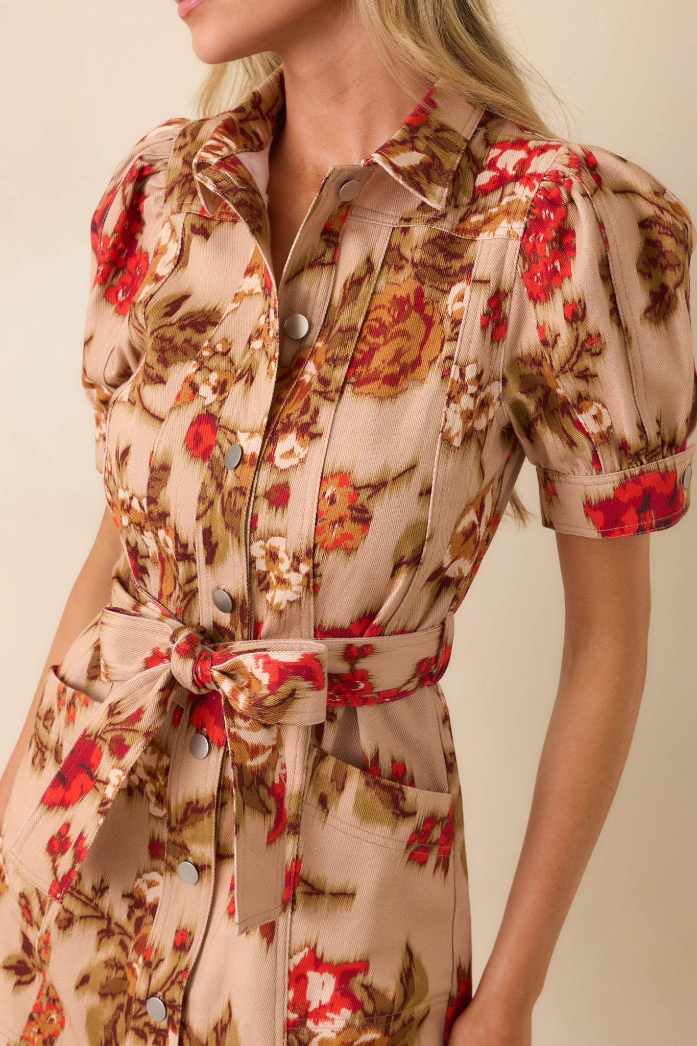 Close-up of tan fabric with red floral print, silver button, and textured panel detail.
