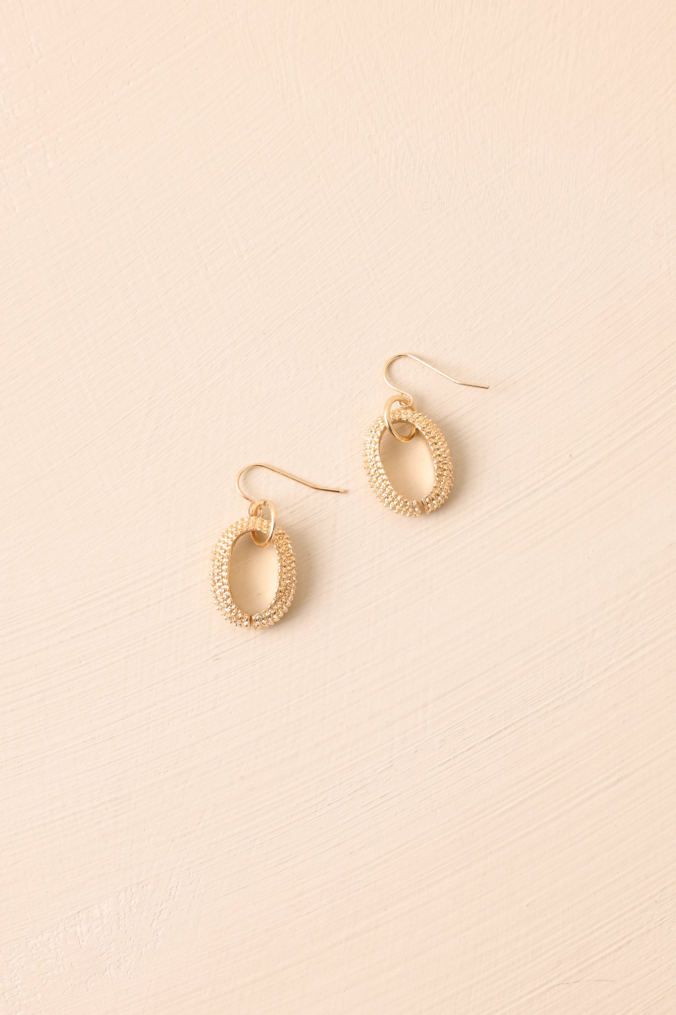 Textured oval hoop earrings styled against a beige backdrop, capturing the elegant drop silhouette.