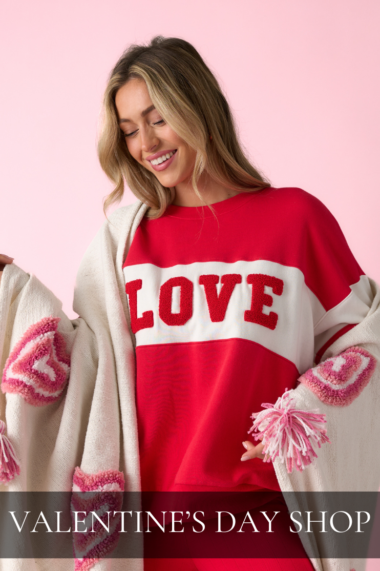 Model wearing a red LOVE graphic sweatshirt layered with a cream heart-detail cardigan, styled for a Valentine’s Day Shop women’s clothing collection.